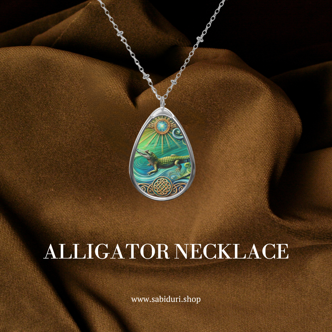 An alligator pendant necklace resting on rich dark brown fabric. The pendant highlights an alligator in a dynamic water setting with vibrant colors and detailed accents, symbolizing resilience and adaptability. The text below reads "ALLIGATOR Necklace" with the website "www.sabiduri.shop.