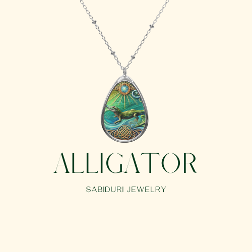 A silver necklace featuring a vibrant alligator pendant displayed on a minimalist cream-colored background. The pendant depicts an alligator with flowing water motifs and celestial symbols. The text reads "ALLIGATOR Sabiduri Jewelry.