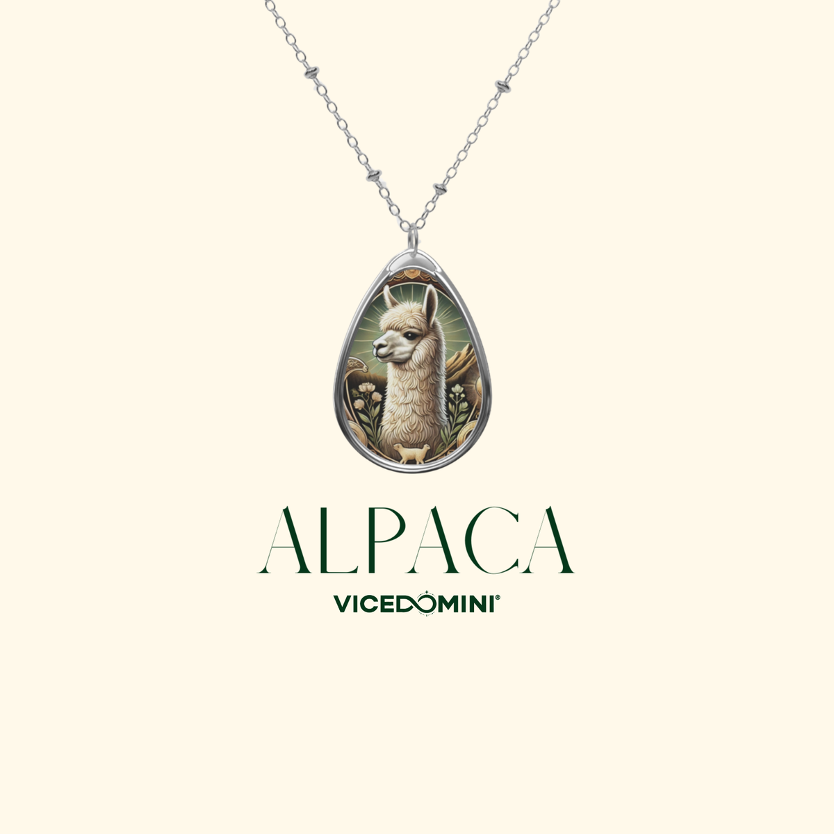 A silver teardrop pendant necklace featuring an illustrated alpaca in the center, shown on a cream background with the text 'ALPACA VICEDOMINI' below.