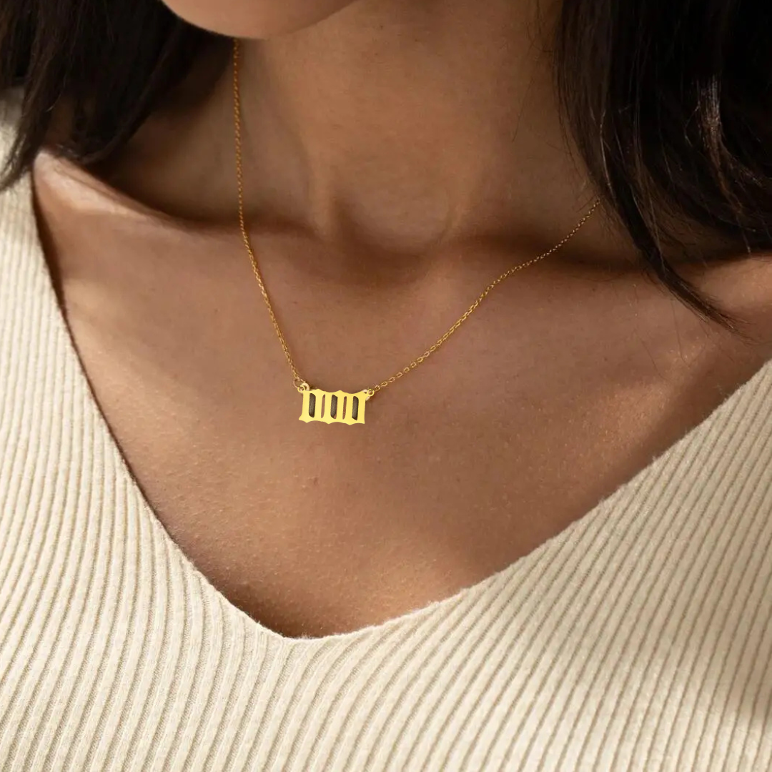 A gold angel number 000 necklace elegantly resting on a woman’s collarbone, complementing her beige knit top. The pendant's sleek, geometric design symbolizes alignment and spiritual awakening.