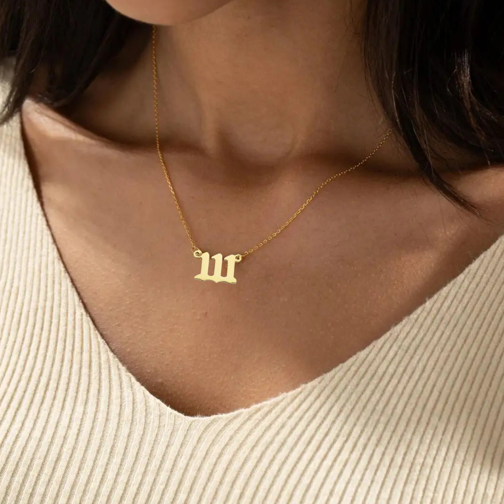 A gold angel number 111 necklace elegantly resting on a woman’s collarbone, complementing her beige knit top. The pendant’s unique design and delicate gold chain add a touch of sophistication.