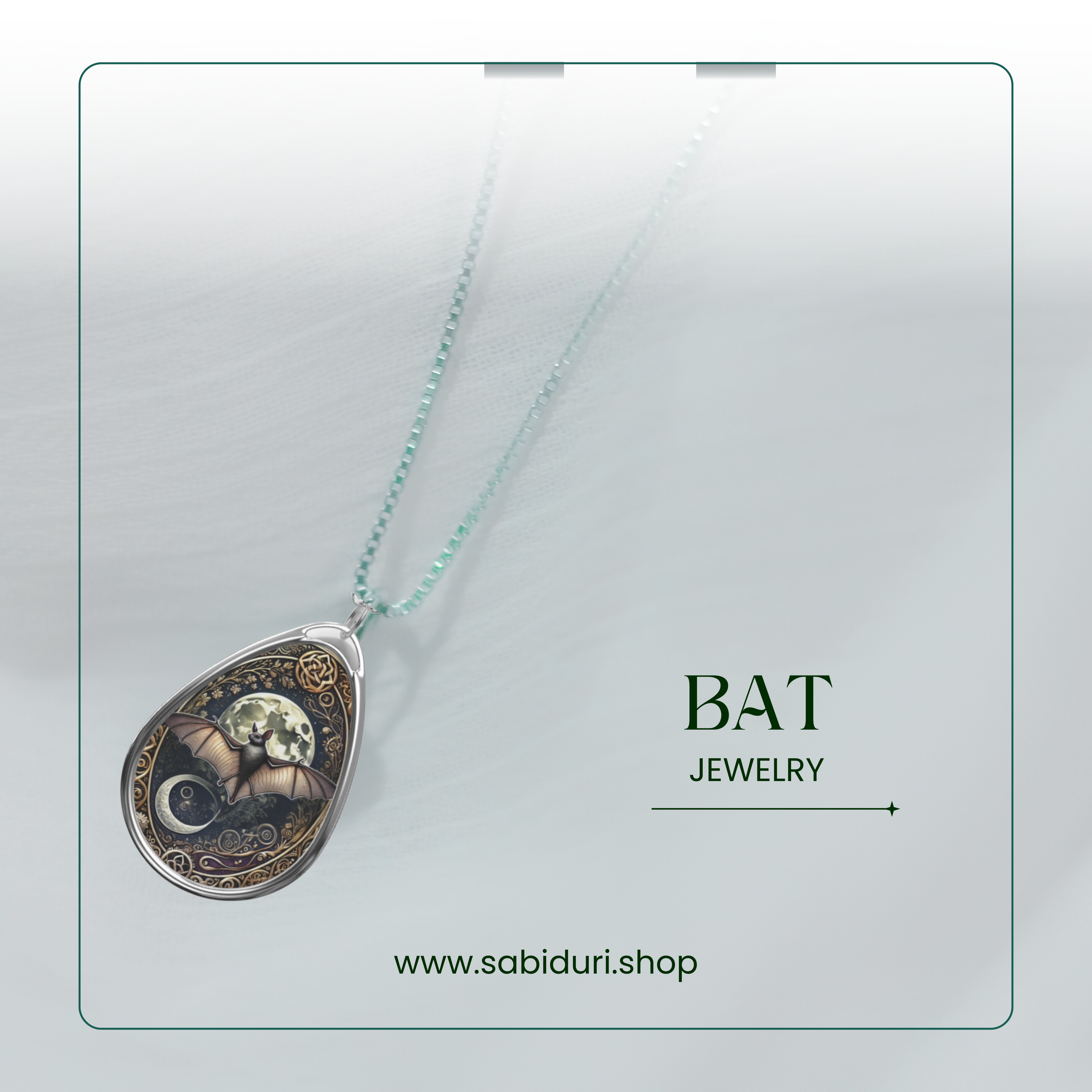 A silver bat pendant necklace placed on a textured white background. The pendant displays a bat in flight against a glowing full moon, framed by ornate golden designs with celestial symbols below. The text reads "BAT Jewelry" and the website "www.sabiduri.shop" is displayed at the bottom.