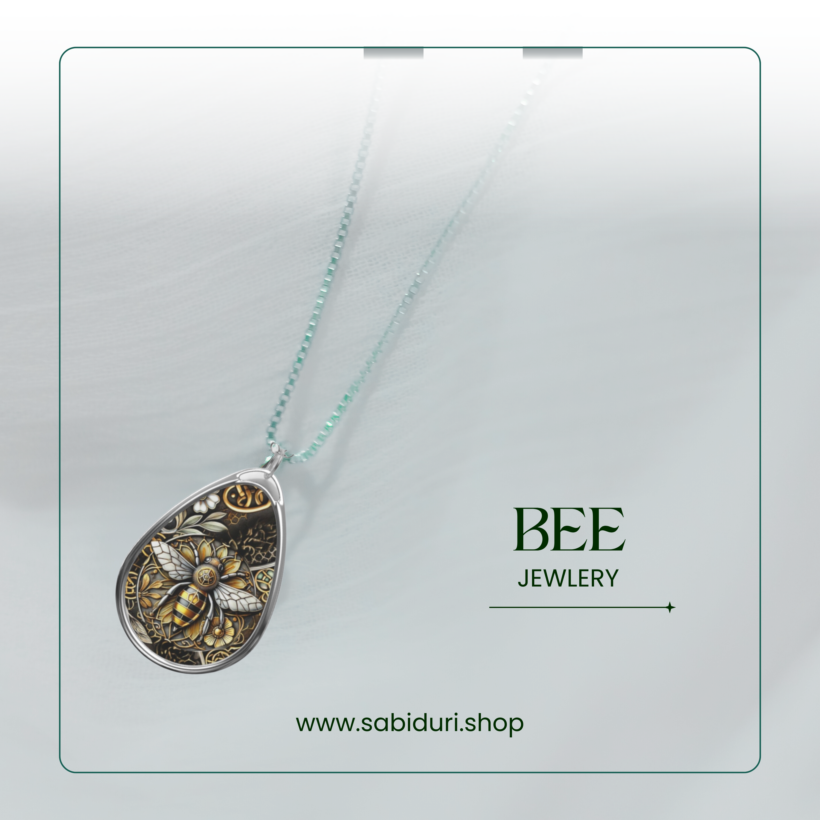 A close-up of a teardrop-shaped pendant featuring an intricate bee design surrounded by floral and geometric elements in gold and black. The necklace is displayed against a soft, white textured background with green text that reads "BEE JEWELRY" and the URL "www.sabiduri.shop" at the bottom, framed by a thin green border.