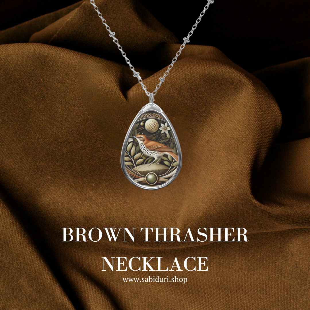 A Brown Thrasher spirit animal necklace draped against a rich brown fabric, highlighting the pendant's vibrant artwork and delicate chain in a luxurious setting.