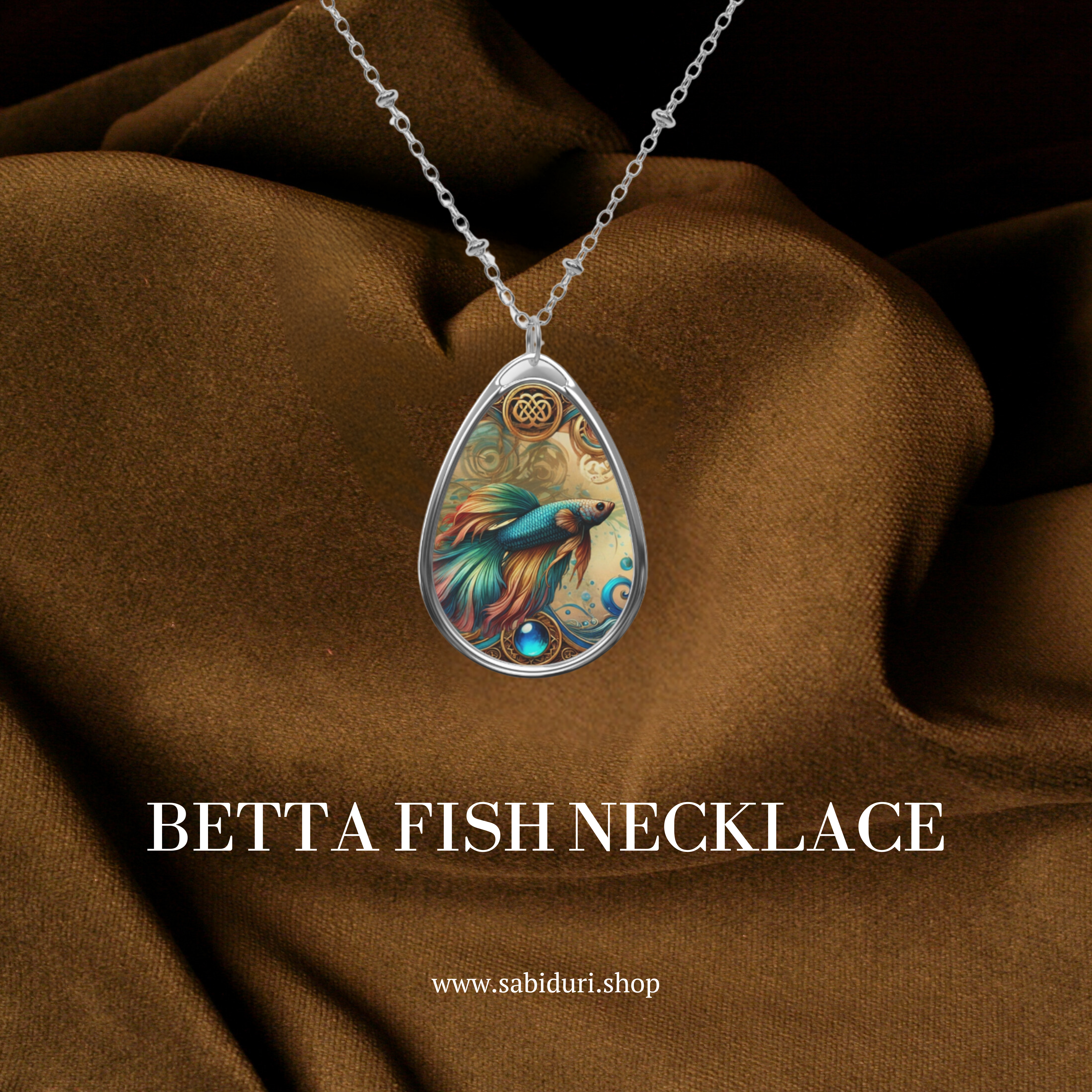 A Betta Fish necklace lying on luxurious brown fabric. The pendant design highlights a vivid Betta Fish with elegant swirls and a gemstone detail, exuding sophistication and artistic beauty.