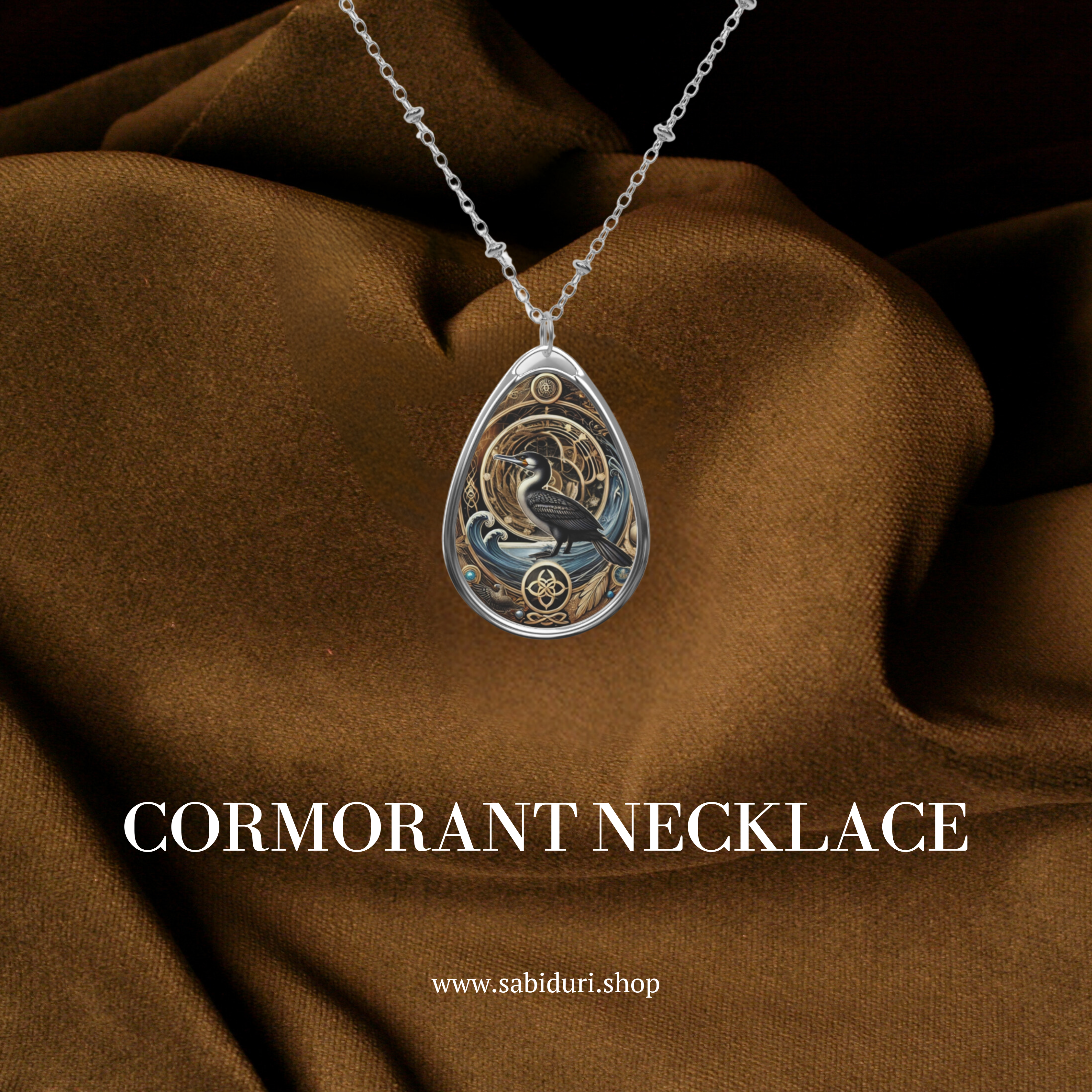 A close-up of the cormorant necklace displayed on rich brown fabric. The pendant showcases a black cormorant against a golden background with swirling waves and celestial details. The text "CORMORANT NECKLACE" and "www.sabiduri.shop" is displayed, enhancing the promotional appeal.