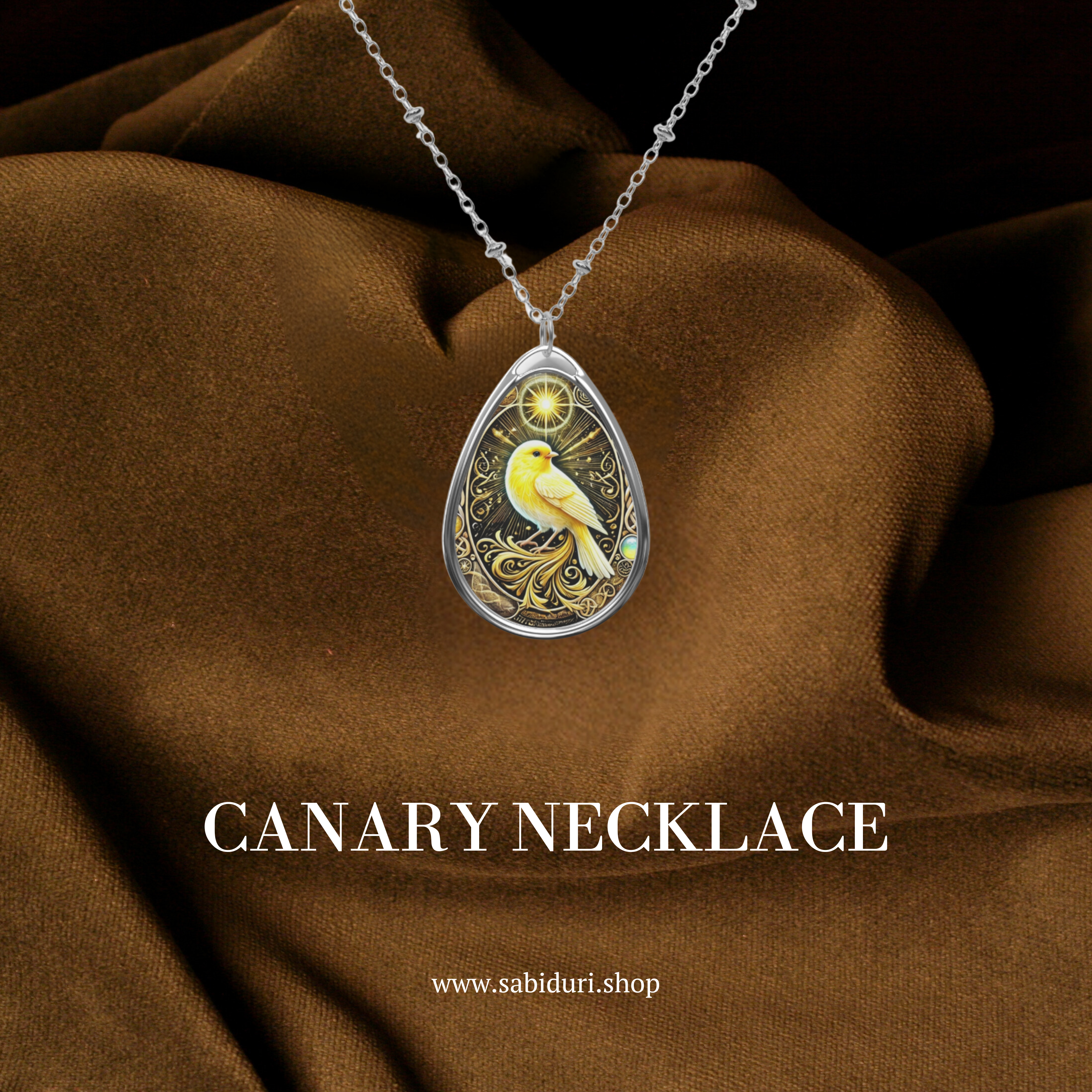 A close-up of a Canary Necklace displayed on a rich brown fabric. The teardrop pendant showcases a golden canary with a celestial glow, surrounded by intricate filigree details, symbolizing freedom and positivity.