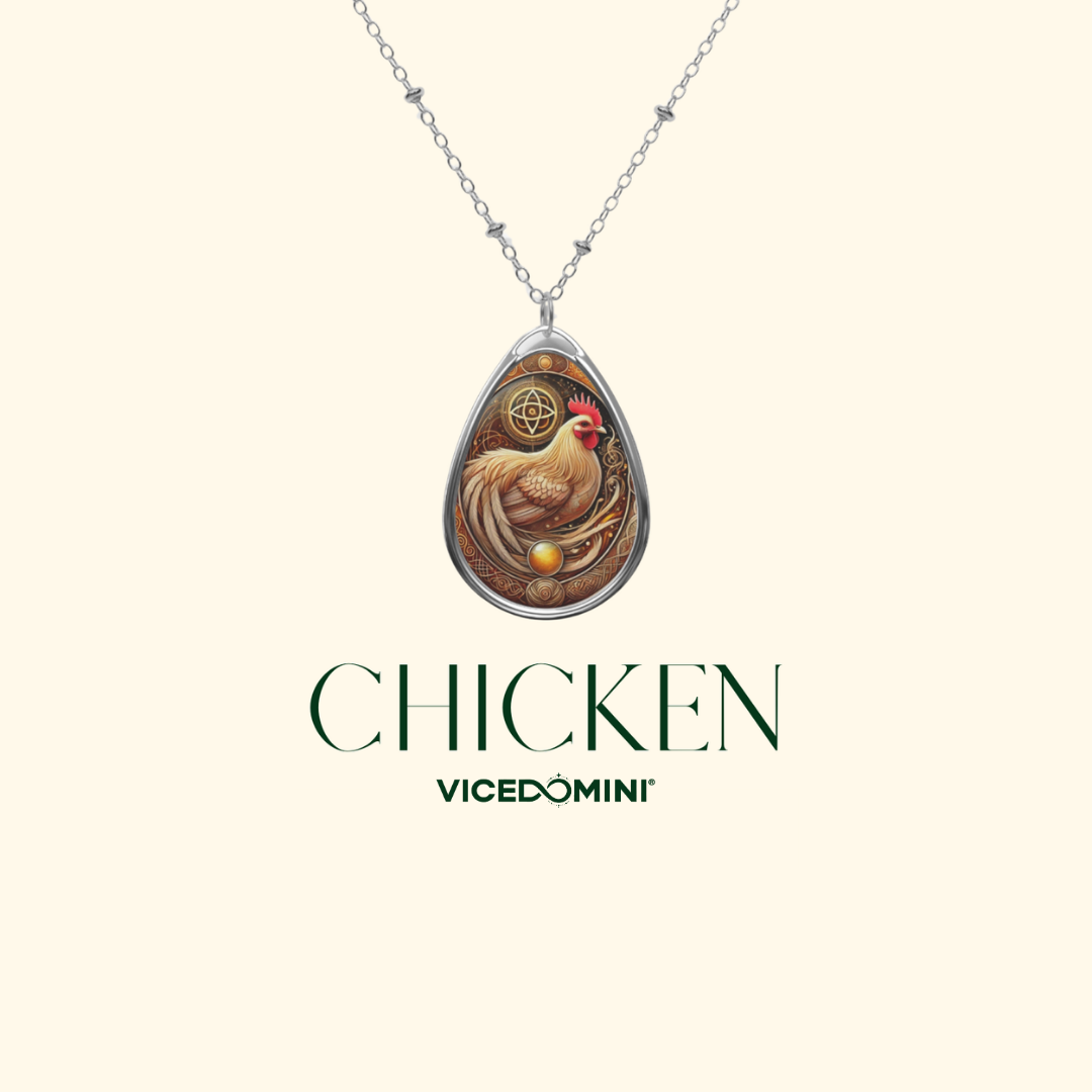 A silver teardrop pendant necklace featuring an illustrated rooster and egg design, displayed on a cream background with the text 'CHICKEN' and 'VICEDOMINI' underneath.
