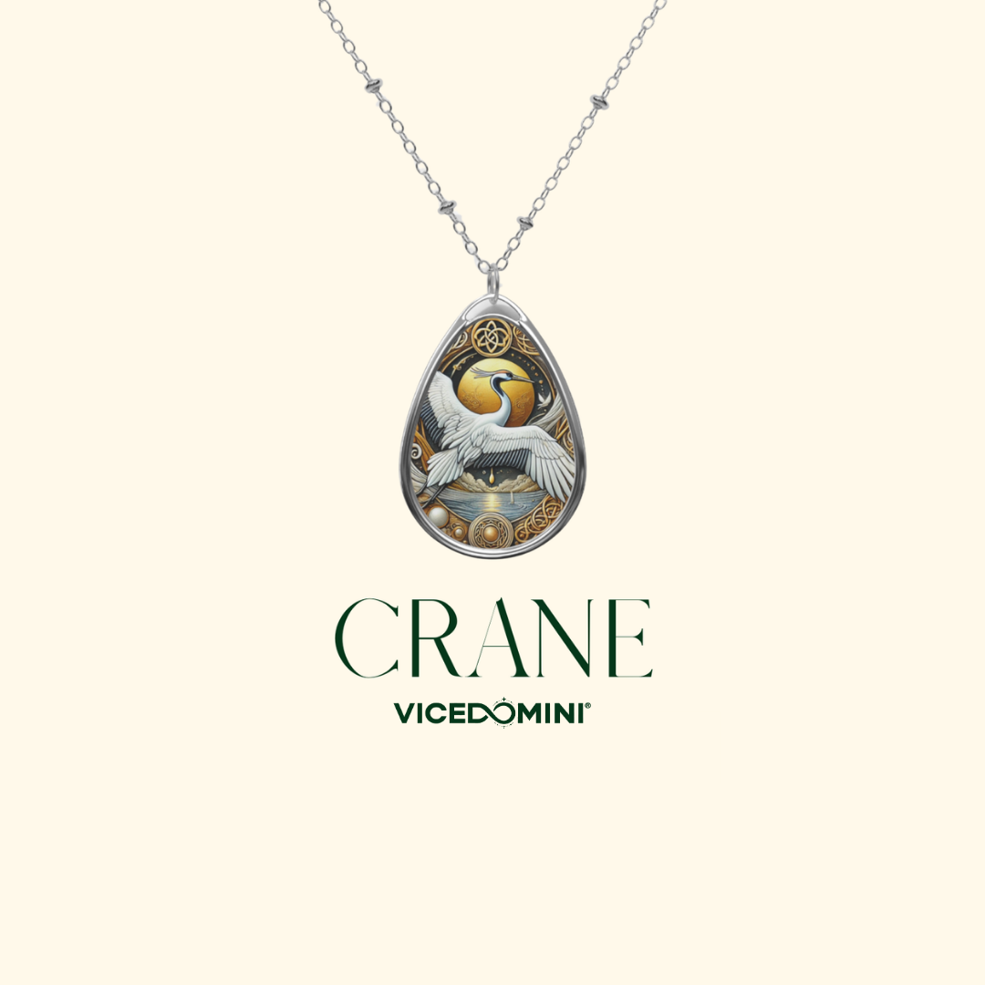 A teardrop-shaped pendant necklace featuring a detailed crane illustration with gold, white, and silver tones, suspended from a silver chain on a light cream background. The brand name 'CRANE' and 'VICEDOMINI' are printed below the pendant.
