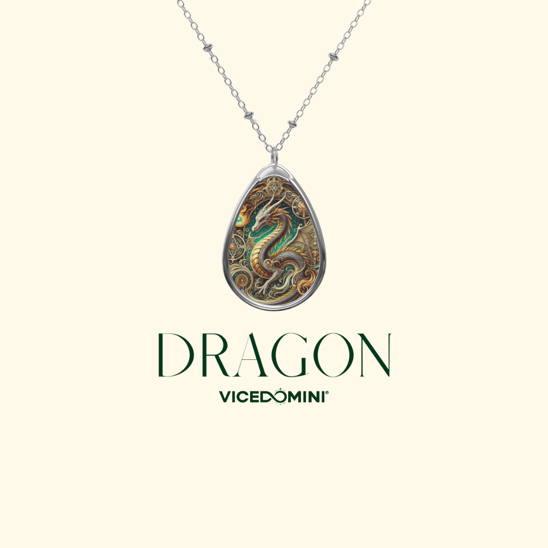 A silver teardrop pendant necklace featuring an intricately detailed dragon illustration in gold, green, and brown tones, displayed on a light cream background with the text 'DRAGON VICEDOMINI' underneath.