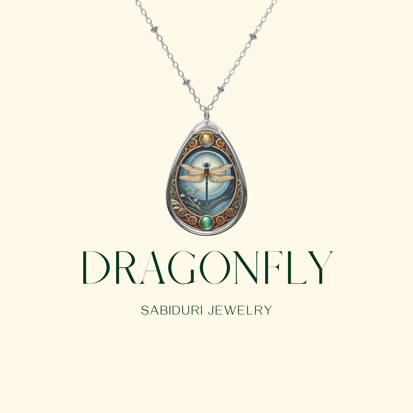 A silver dragonfly necklace pendant is displayed on a minimalist cream-colored background. The pendant features a detailed dragonfly with a glowing sky and intricate scrollwork in gold with a green gemstone at the base. The text reads "DRAGONFLY Sabiduri Jewelry.