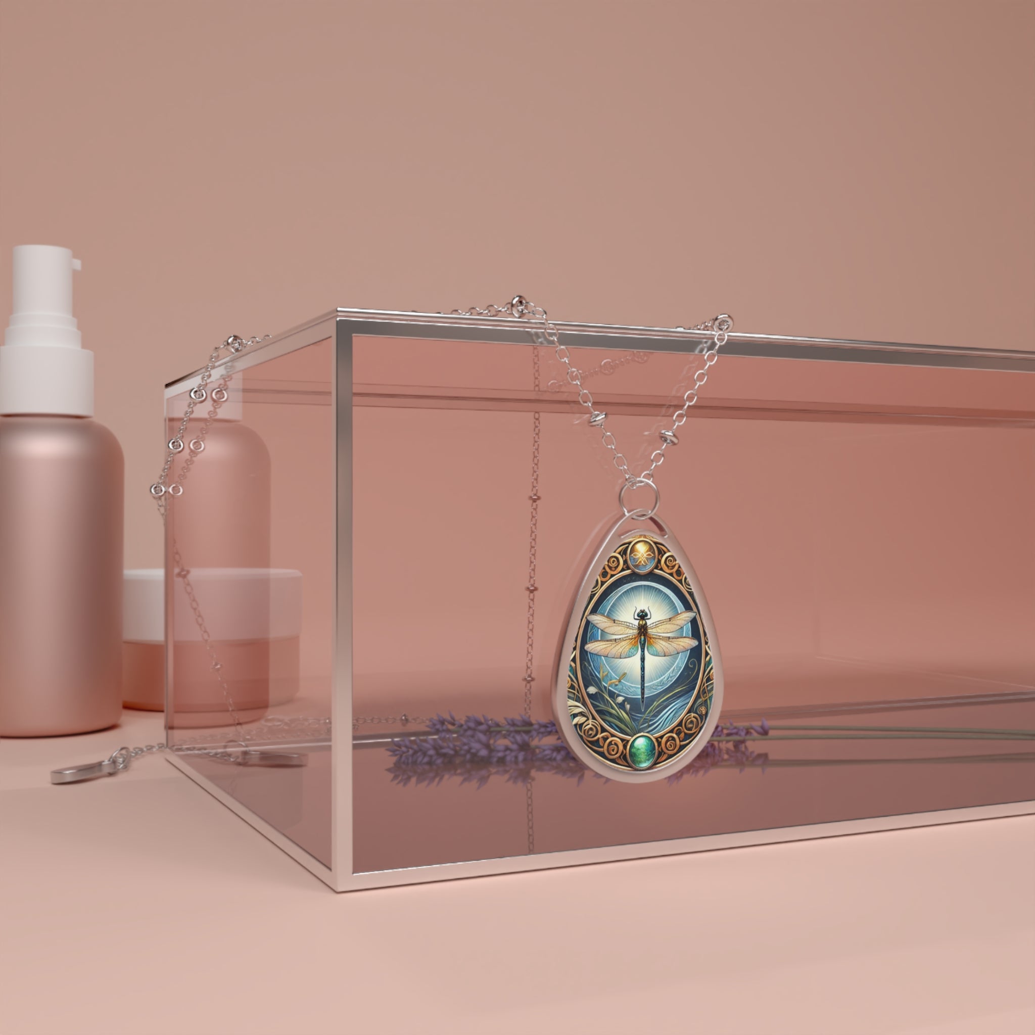 A silver necklace featuring a dragonfly pendant draped over a transparent box with lavender sprigs and cosmetic bottles in the background, set against a soft pink backdrop. The pendant depicts a dragonfly with a glowing background of the sky, surrounded by ornate patterns, and accented with green gemstones.