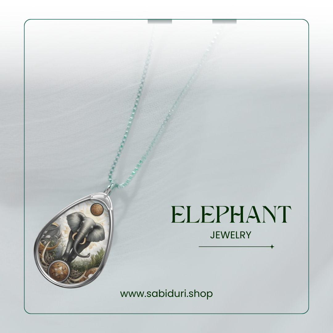 A silver elephant pendant necklace displayed on a soft white background. The pendant depicts a regal elephant surrounded by nature and celestial designs, representing power and tranquility. The text reads "ELEPHANT Jewelry" along with the website "www.sabiduri.shop.
