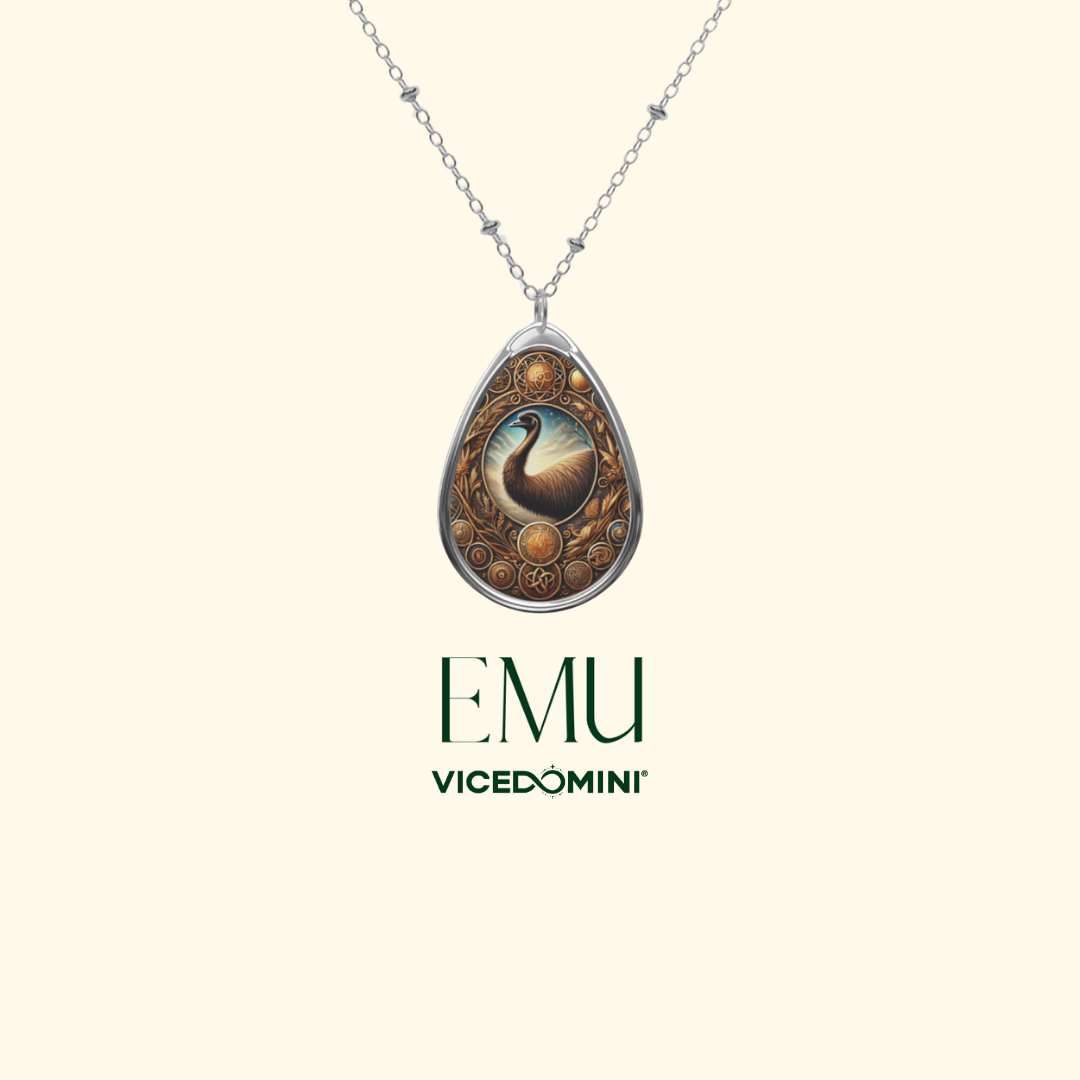 A teardrop-shaped pendant necklace with a silver-toned chain, featuring an ornate circular design with a central peacock illustration and the text 'EMU VICEDOMINI' below on a light cream background.