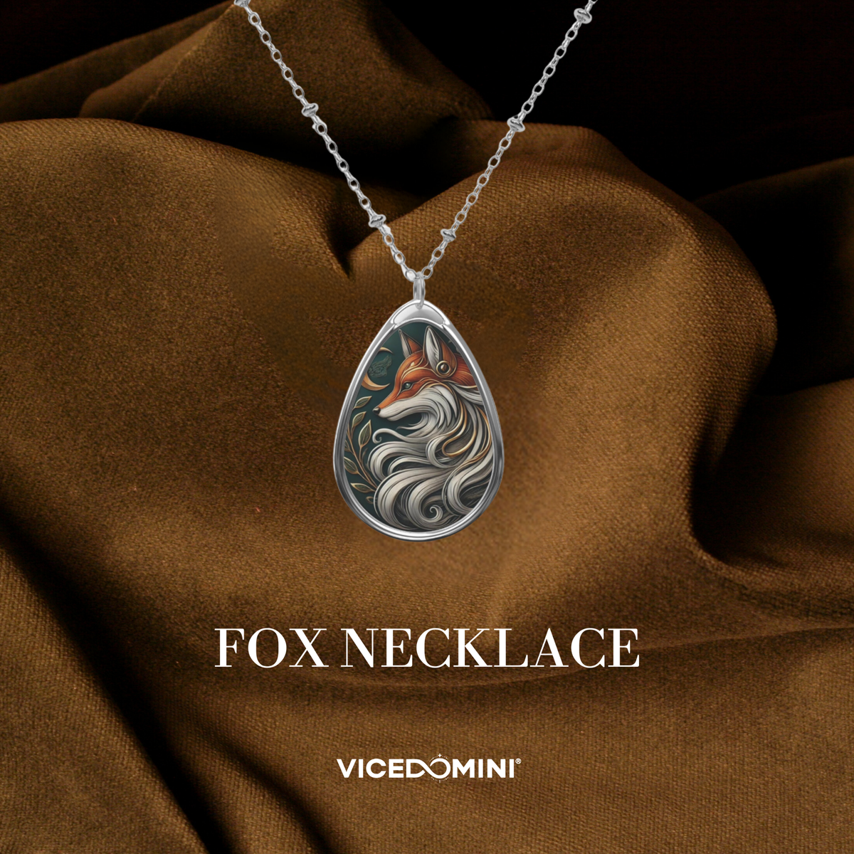 A teardrop-shaped silver pendant necklace featuring an illustrated fox with flowing white and gray fur details, displayed on draped brown fabric with the text 'FOX NECKLACE' and 'VICEDOMINI' below.