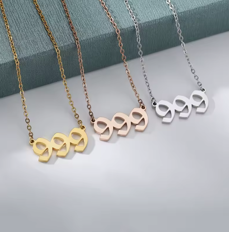 Three angel number 999 necklaces displayed on a soft surface, available in gold, silver, and rose gold finishes. Each necklace features a sleek, modern pendant with a delicate chain, symbolizing luck, spiritual alignment, and divine guidance. The polished metal tones reflect light, highlighting their elegant and meaningful design.
