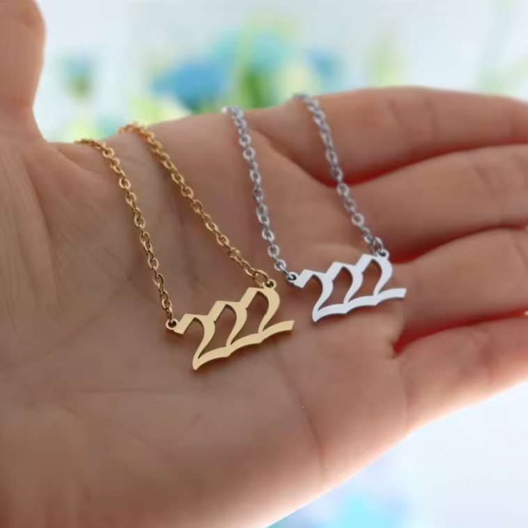 A close-up of a hand holding two angel number 222 necklaces—one in gold and one in silver. The modern pendant design and polished finish reflect light, emphasizing their elegant style.