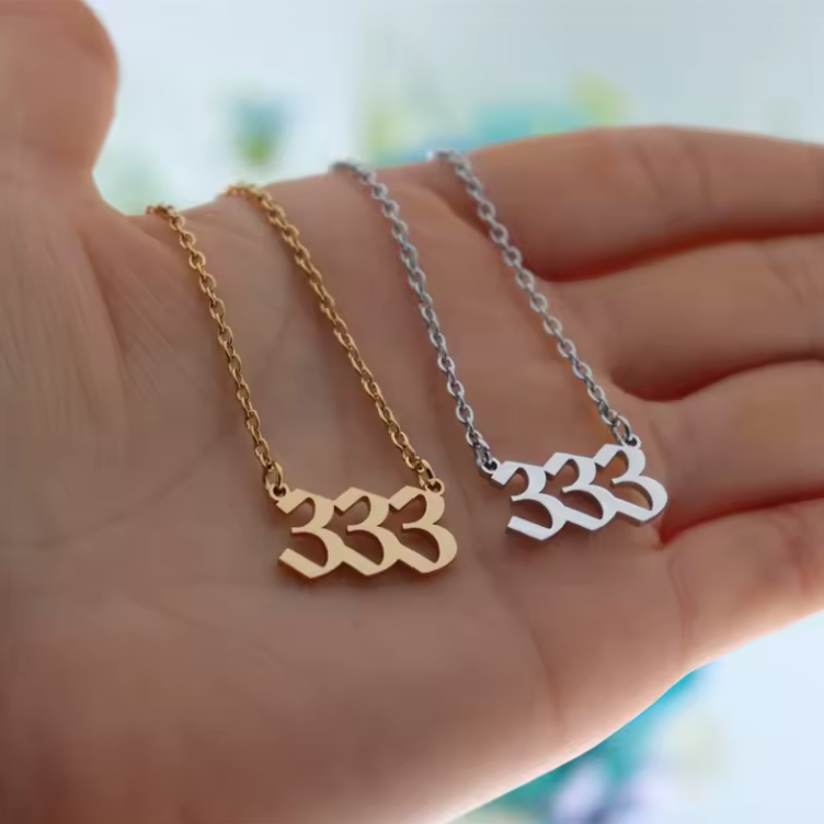 A close-up of a hand holding two angel number 333 necklaces—one in gold and one in silver. The modern pendant design and polished finish reflect light, emphasizing their elegant style.