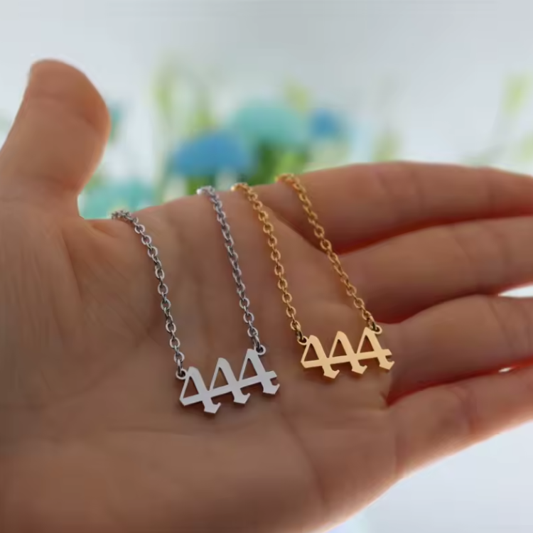 A close-up of a hand holding two angel number 444 necklaces—one in gold and one in silver. The modern pendant design and polished finish reflect light, emphasizing their elegant style.