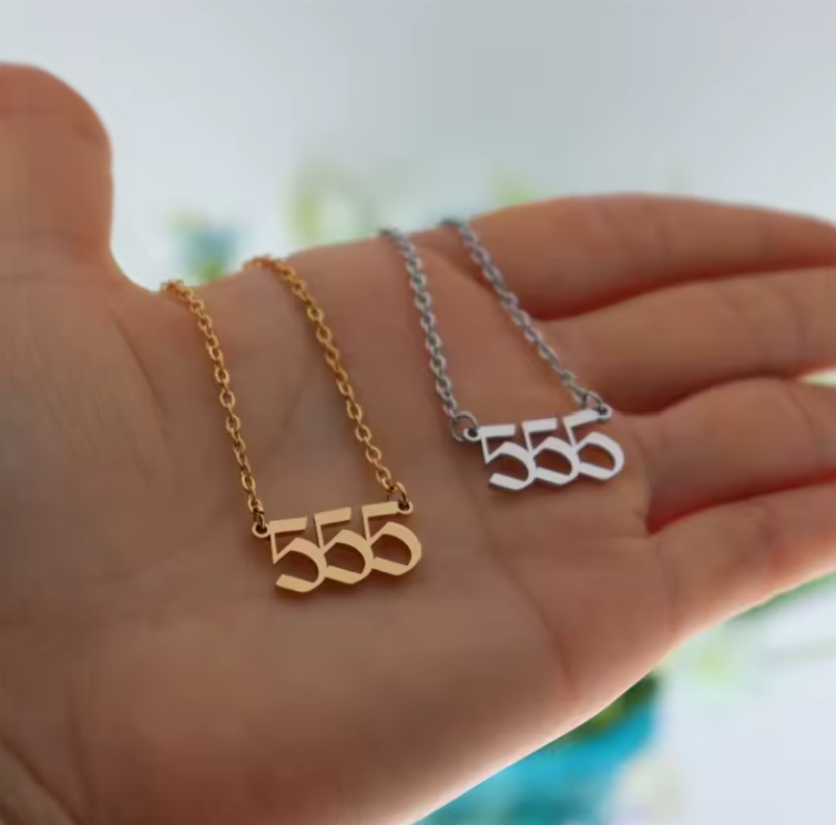 A close-up of a hand holding two angel number 555 necklaces—one in gold and one in silver. The modern pendant design and polished finish reflect light, emphasizing their elegant style.