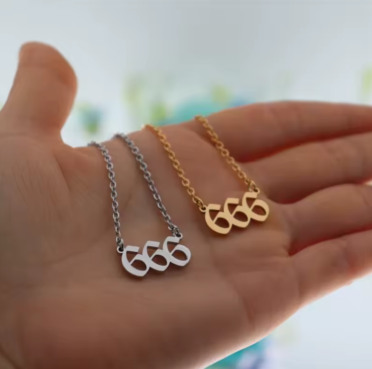 A close-up of a hand holding two angel number 666 necklaces—one in gold and one in silver. The modern pendant design and polished finish reflect light, emphasizing their elegant style.
