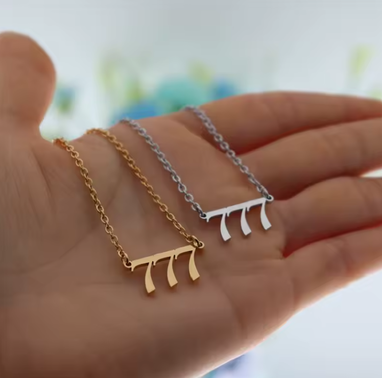A close-up of a hand holding two angel number 777 necklaces—one in gold and one in silver. The modern pendant design and polished finish reflect light, emphasizing their elegant style.