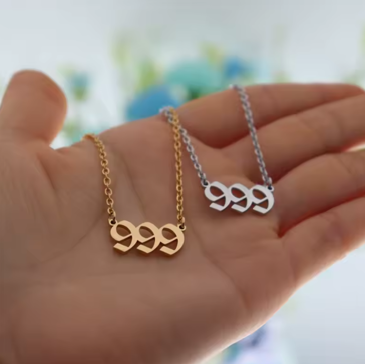 A close-up of a hand holding two angel number 999 necklaces—one in gold and one in silver. The modern pendant design and polished finish reflect light, emphasizing their elegant style.