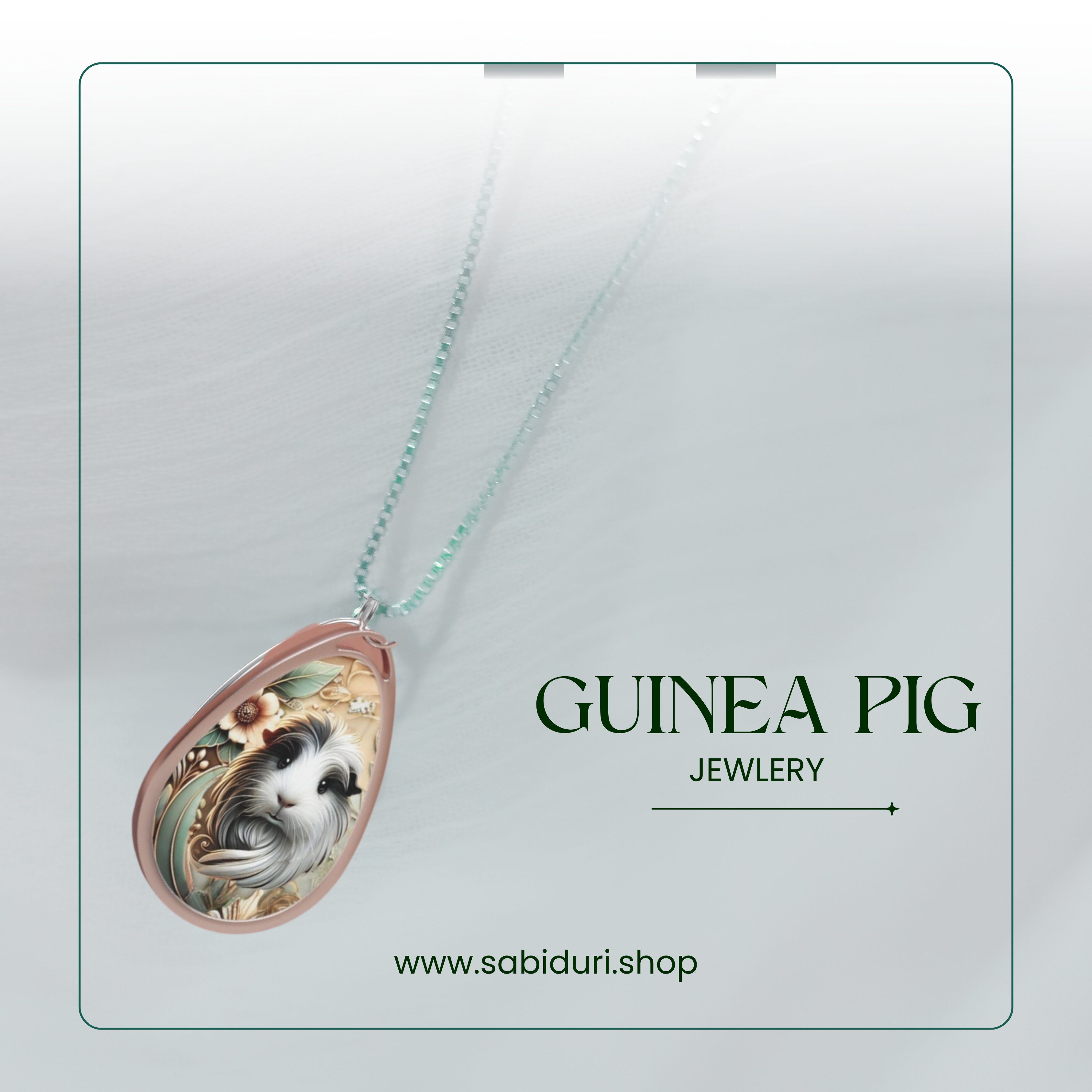 A close-up of the guinea pig necklace pendant, featuring detailed artwork with floral accents. The necklace is displayed against a soft, white textured background with green text that reads "GUINEA PIG JEWELRY" and the URL "www.sabiduri.shop" at the bottom, framed by a thin green border.