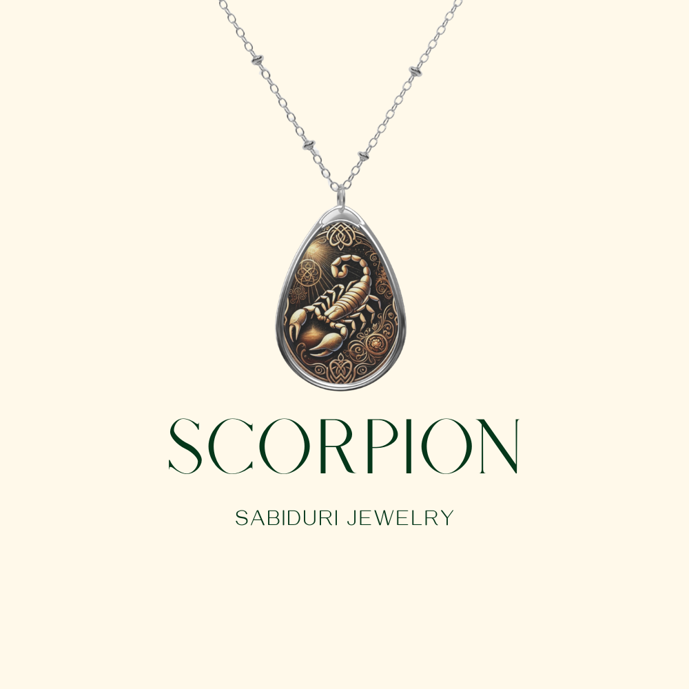 A silver necklace with a teardrop-shaped pendant featuring a detailed scorpion illustration surrounded by ornate patterns. The pendant is displayed on a neutral background, with the text "SCORPION" and "SABIDURI JEWELRY" elegantly positioned beneath.