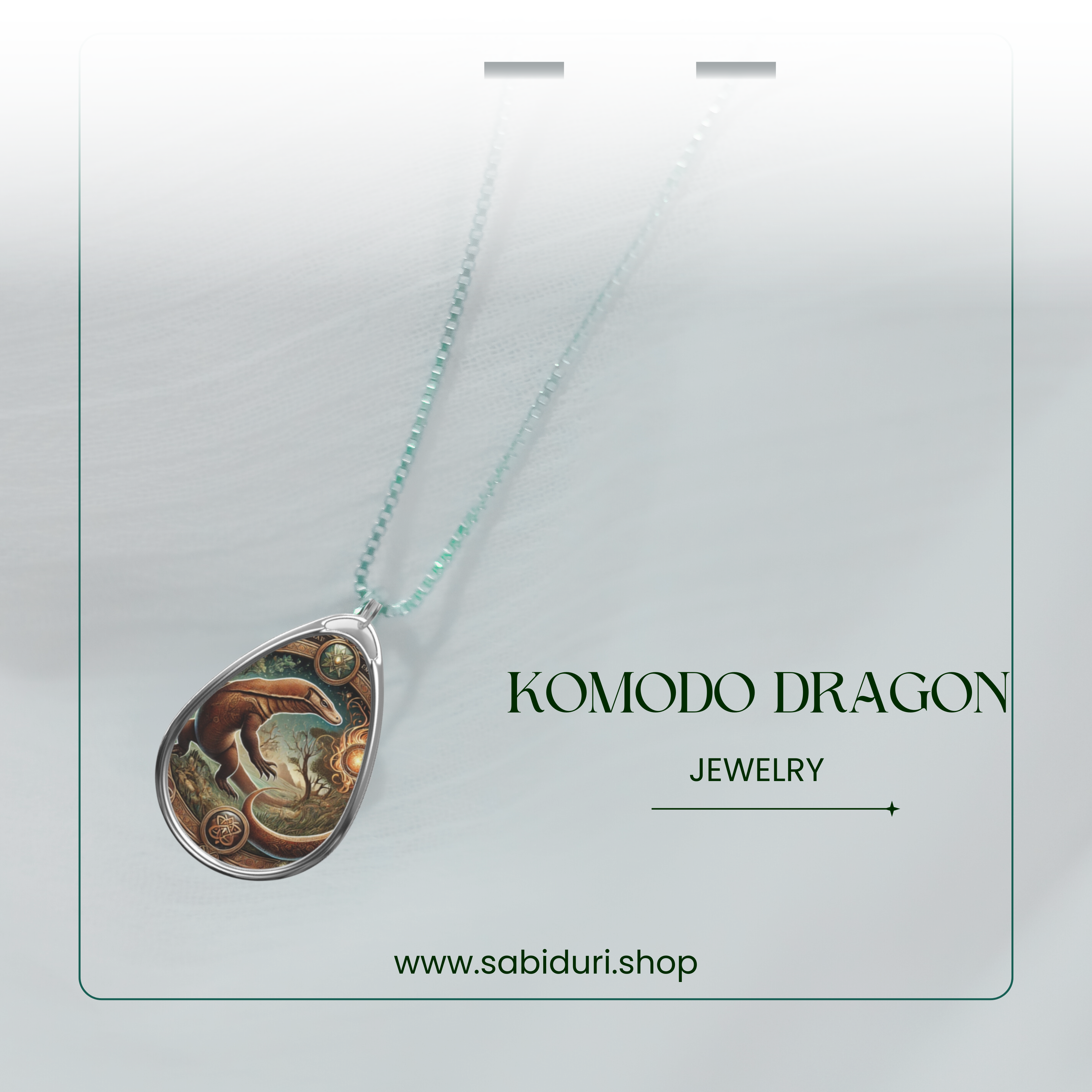 A Komodo dragon spirit animal pendant with an ornate border, showcased on a soft gradient background with a sparkling chain. "Komodo Dragon Jewelry" and "www.sabiduri.shop" are written below.