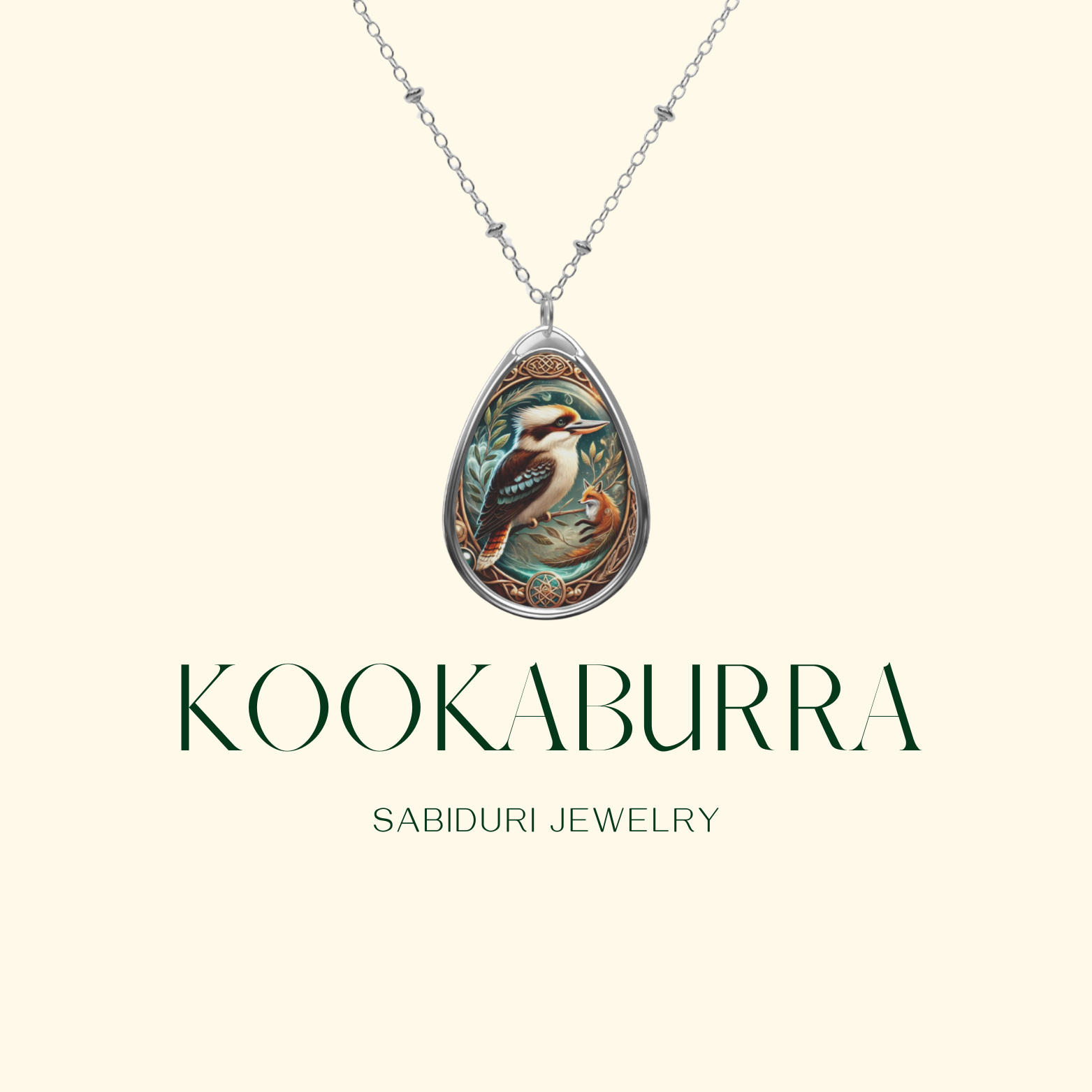 A refined silver pendant with an illustration of a kookaburra, encased in an elegant teardrop-shaped frame with ornamental detailing. The pendant hangs from a dainty silver chain against a soft beige background. The text "KOOKABURRA" and "SABIDURI JEWELRY" is displayed in a stylish font.
