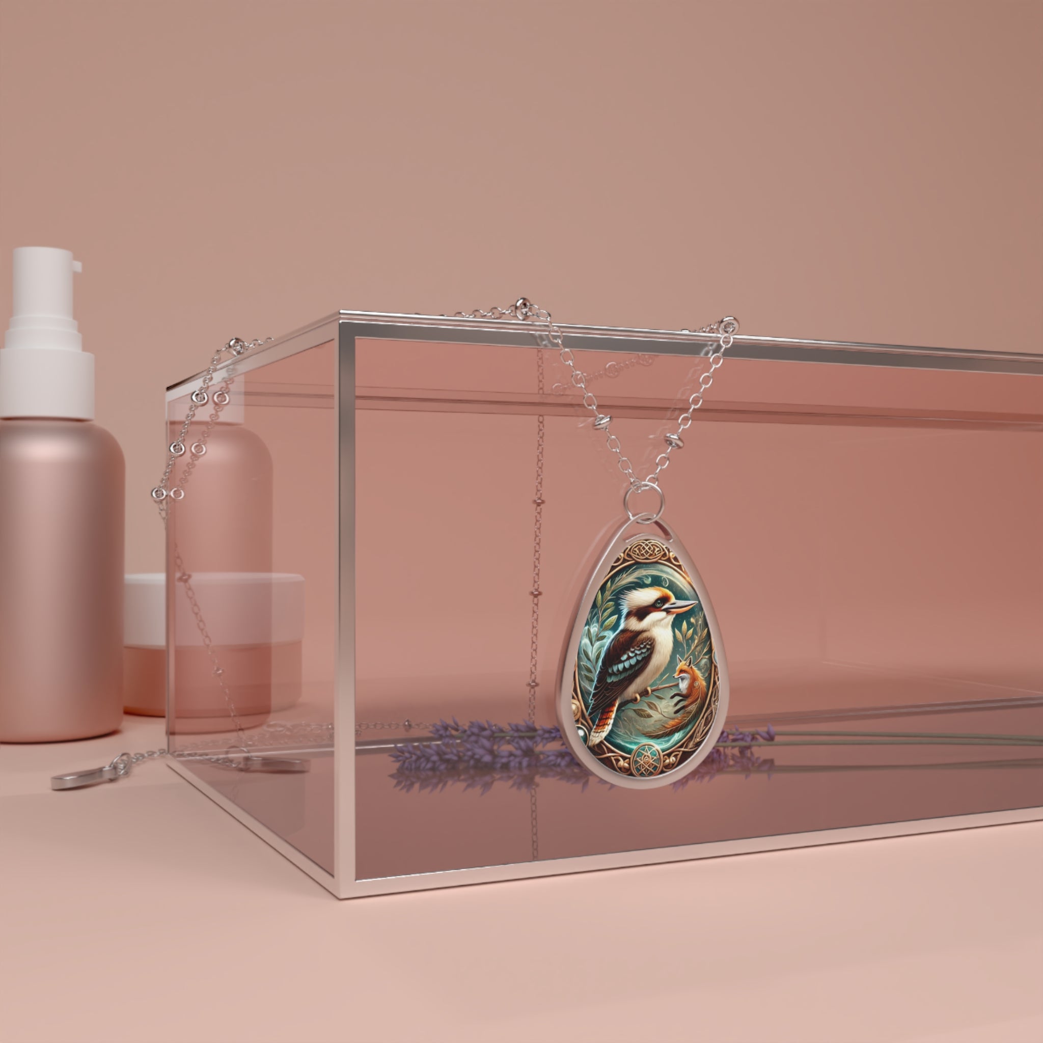 A close-up of the kookaburra pendant draped over a transparent glass box, placed in a soft, modern setting with beauty products and lavender in the background. The pendant’s golden embellishments and silver frame contrast beautifully against the soft peach tones.