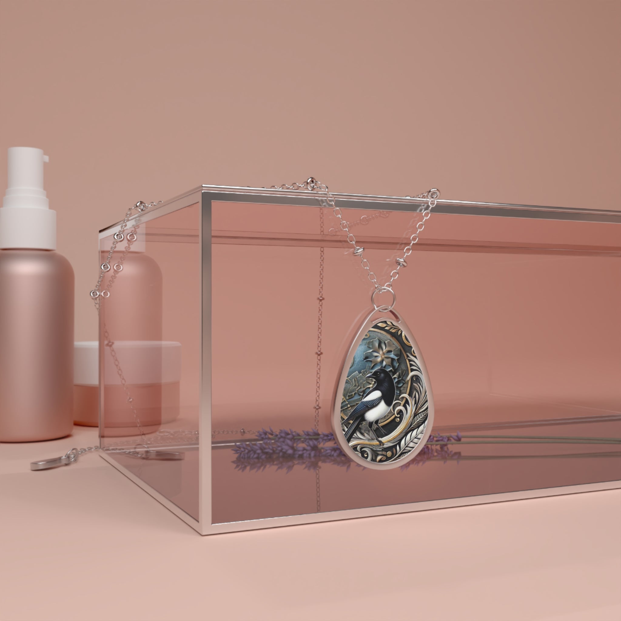 The magpie necklace is elegantly draped over a transparent glass box, with minimalist beauty products in soft pink tones arranged around it. Lavender sprigs are visible under the glass, adding a natural element to the scene.
