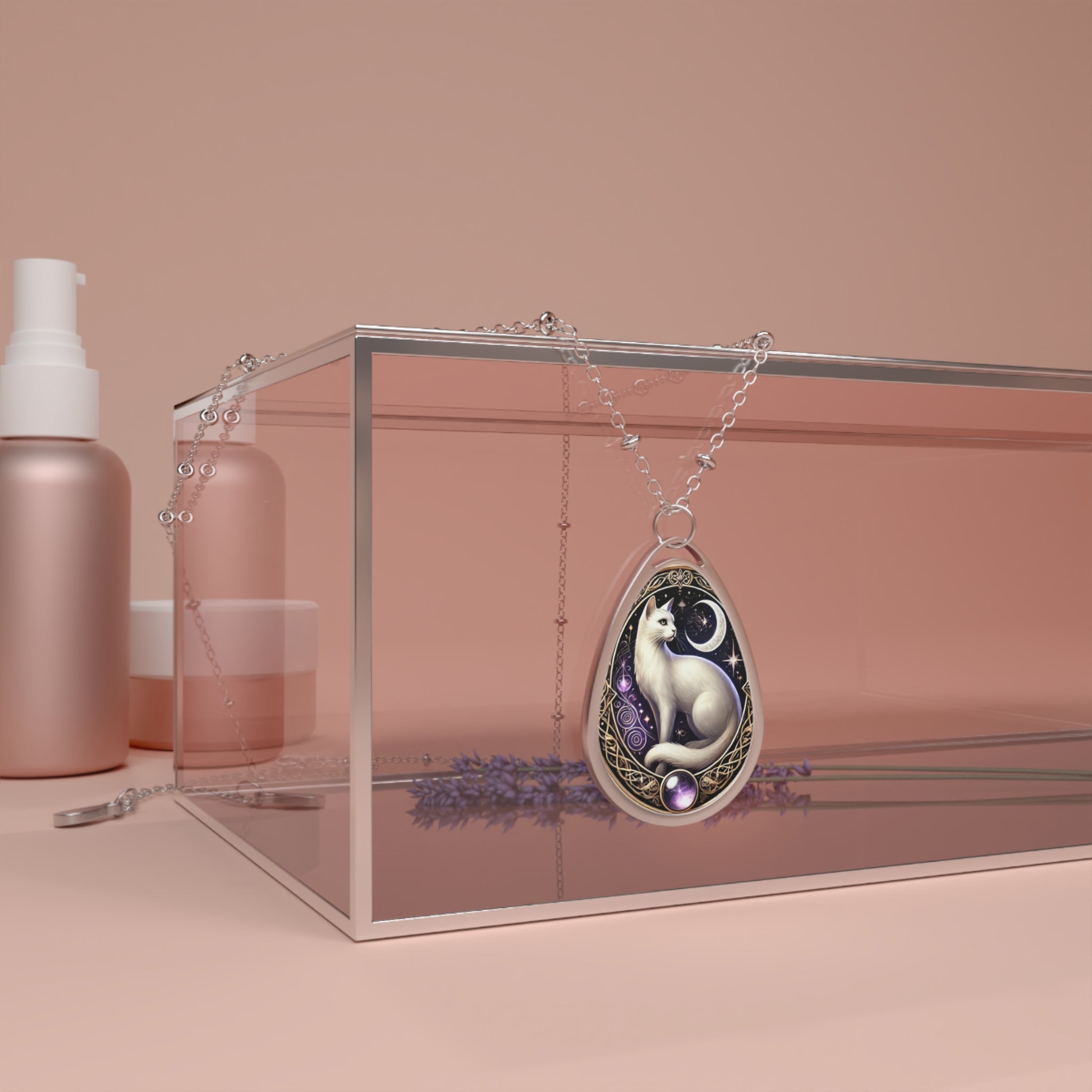 A teardrop-shaped pendant featuring an elegant white cat sitting under a crescent moon, adorned with intricate golden filigree and purple gemstone details. The necklace is draped over a transparent glass box with soft lavender sprigs and beauty products in the background.