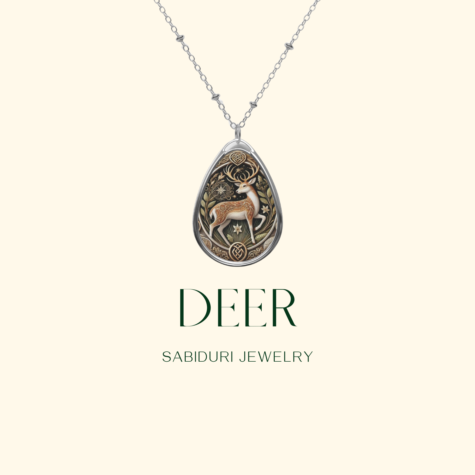 A silver teardrop pendant featuring a stylized deer and floral designs on a clean, light-colored background. The necklace is presented centrally, with the words "DEER SABIDURI JEWELRY" below the image, and the website name subtly placed beneath.