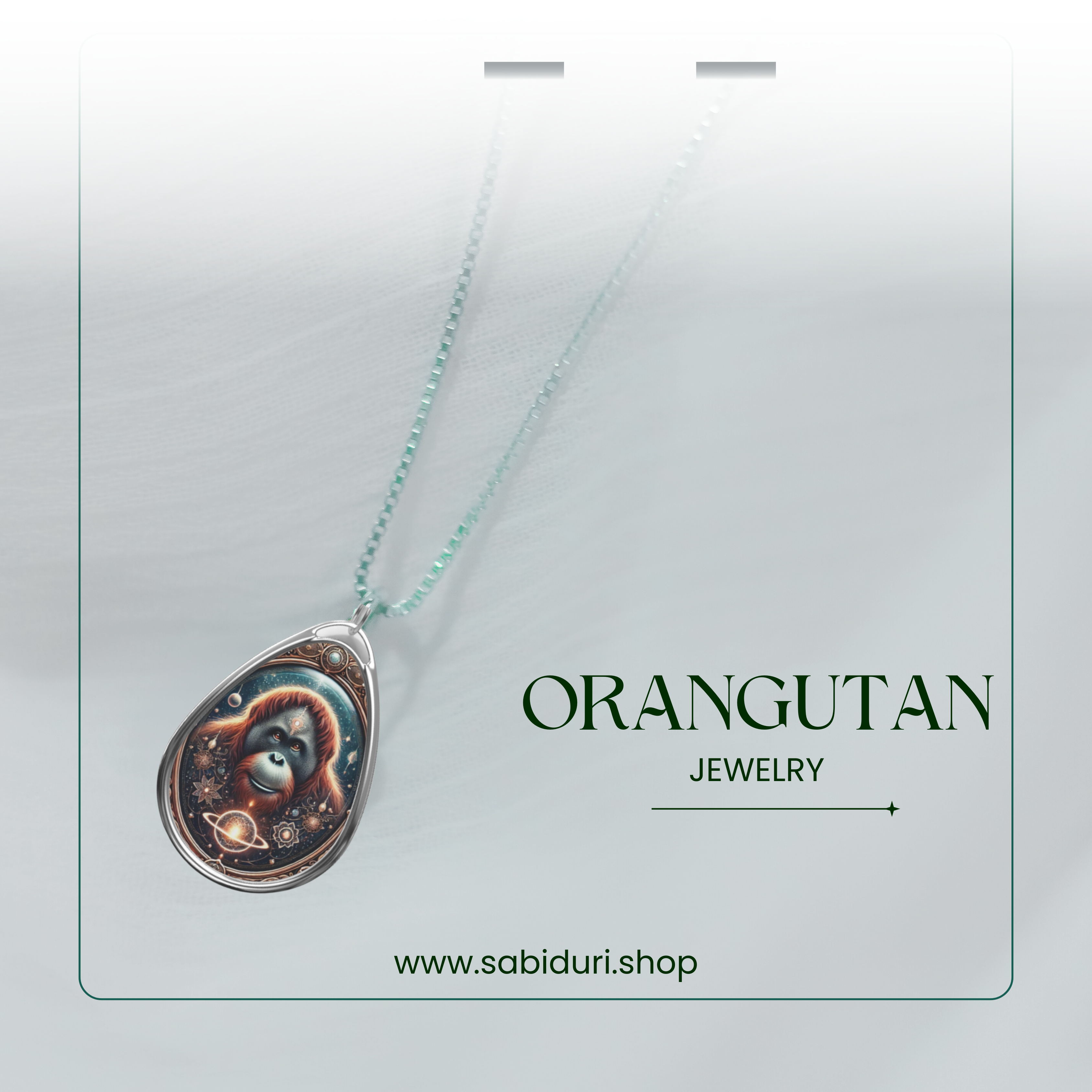 The pendant necklace is suspended against a soft, neutral backdrop, with a delicate chain. The orangutan artwork within the pendant is encased in a silver frame with ornate detailing. Text on the image reads "ORANGUTAN JEWELRY" along with the website "www.sabiduri.shop."