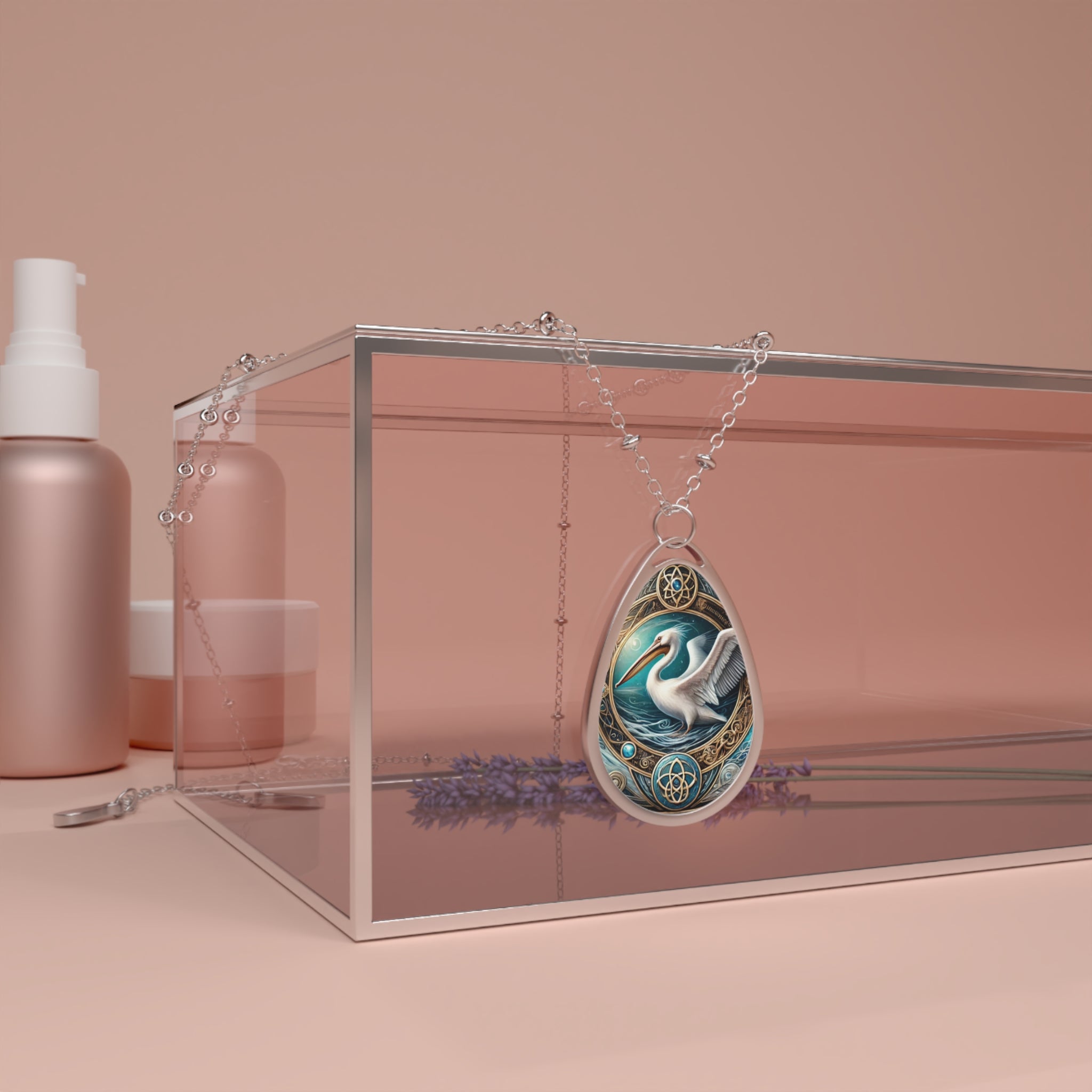 A pelican-themed pendant with intricate gold and blue detailing draped over a clear jewelry display box, placed on a pastel pink surface with a lavender sprig beside it. The pendant exudes elegance and craftsmanship.