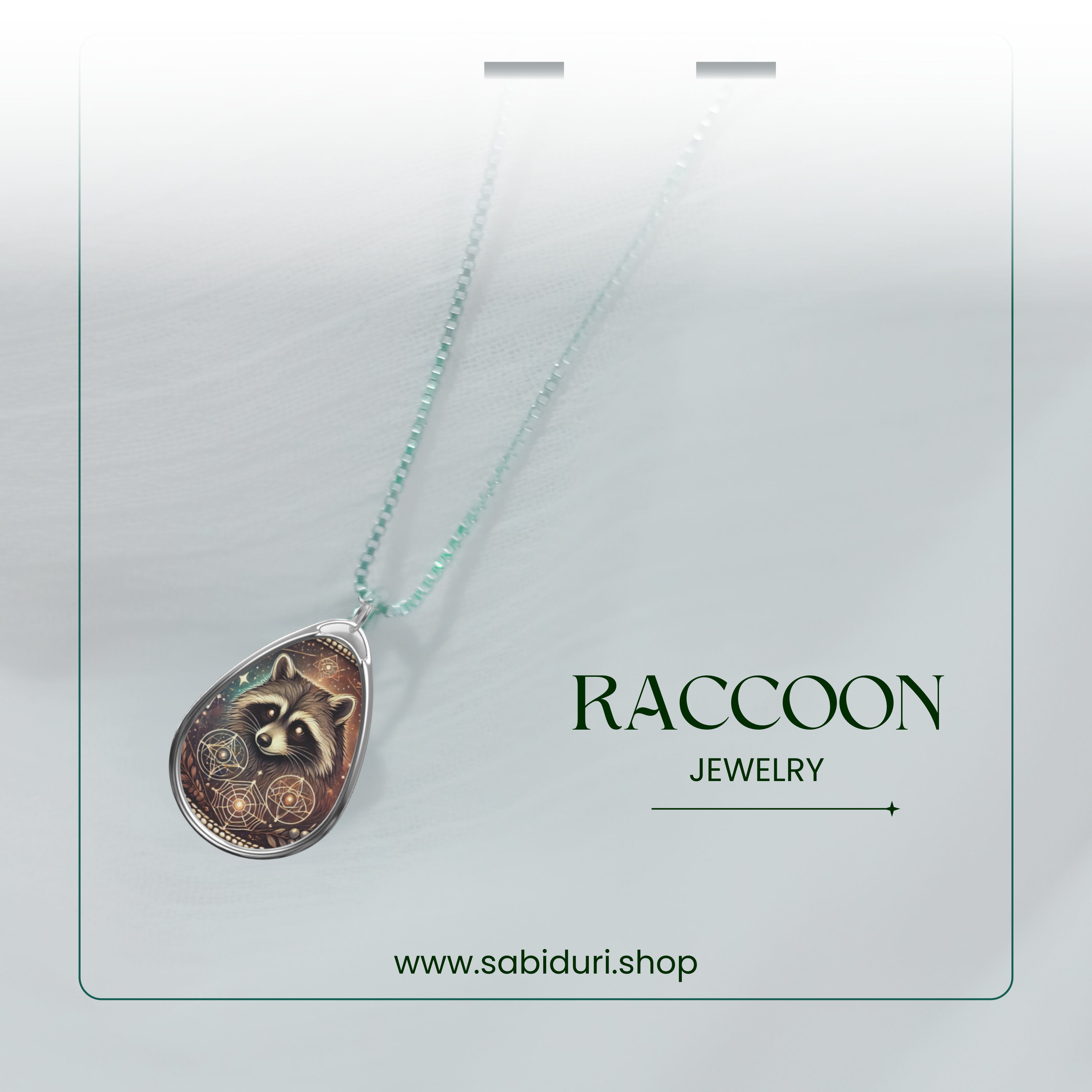 Close-up of a raccoon pendant necklace on a soft white fabric background, with the text 'RACCOON JEWELRY' and 'www.sabiduri.shop' placed beside it.