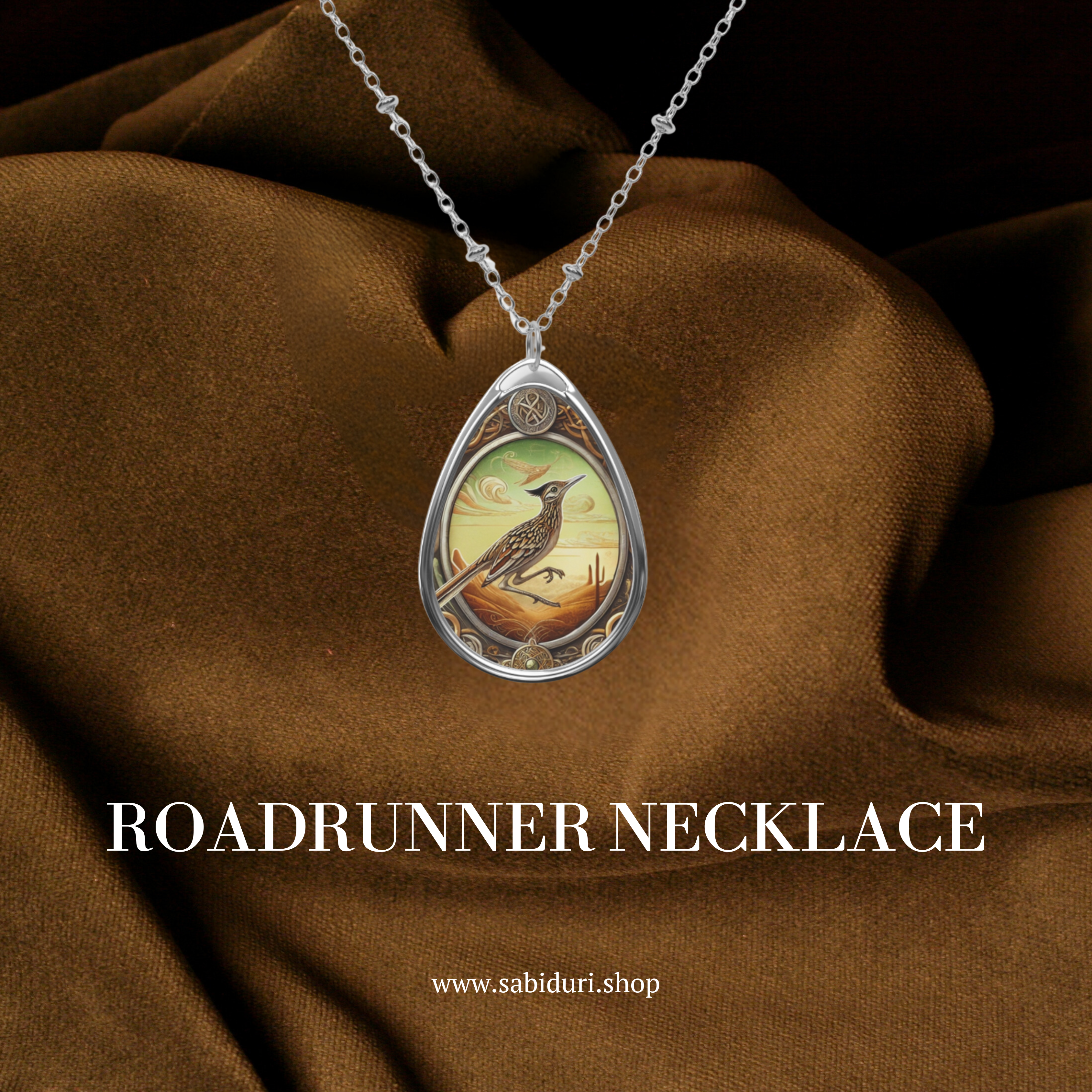 A roadrunner pendant necklace with intricate artwork, placed against a rich brown fabric for a luxurious display. The pendant captures a desert-inspired scene with warm, golden tones and detailed craftsmanship.