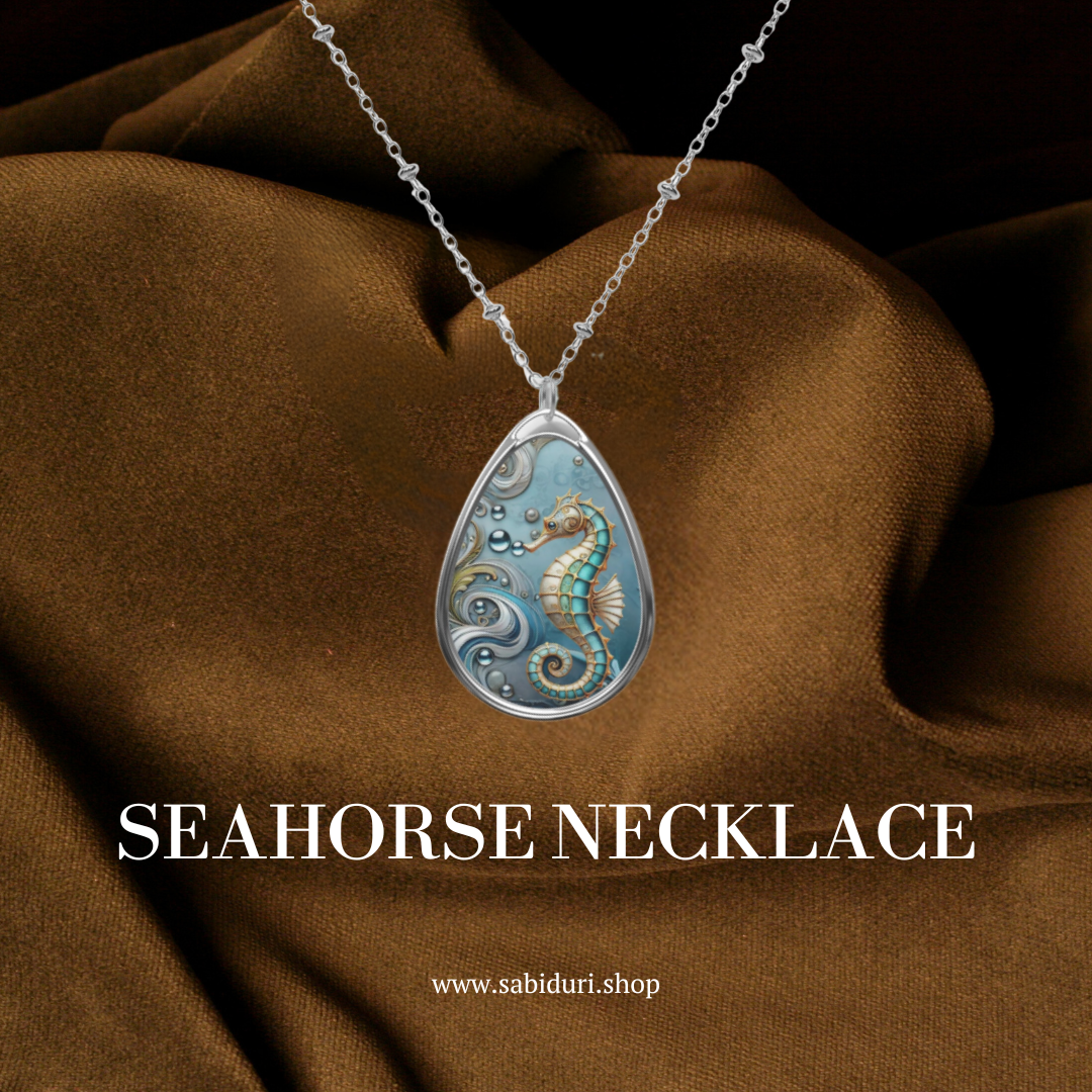 A close-up of the seahorse necklace, showcasing the same intricate pendant design, resting on a rich brown fabric background. The text "SEAHORSE NECKLACE" is prominently displayed in white at the bottom, along with the URL "www.sabiduri.shop."
