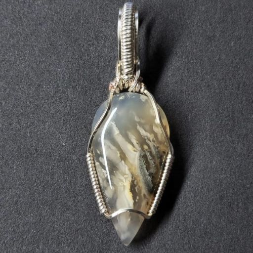 A silver wire-wrapped pendant with a unique, leaf-shaped banded agate stone, its natural patterns resembling a landscape scene, against a grey background.