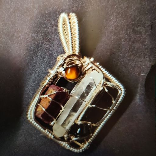 A wire-wrapped pendant featuring a clear quartz center with a smaller amber stone and fragments of garnet, set against a grey backdrop, creating an impression of a miniature, crystalline window.