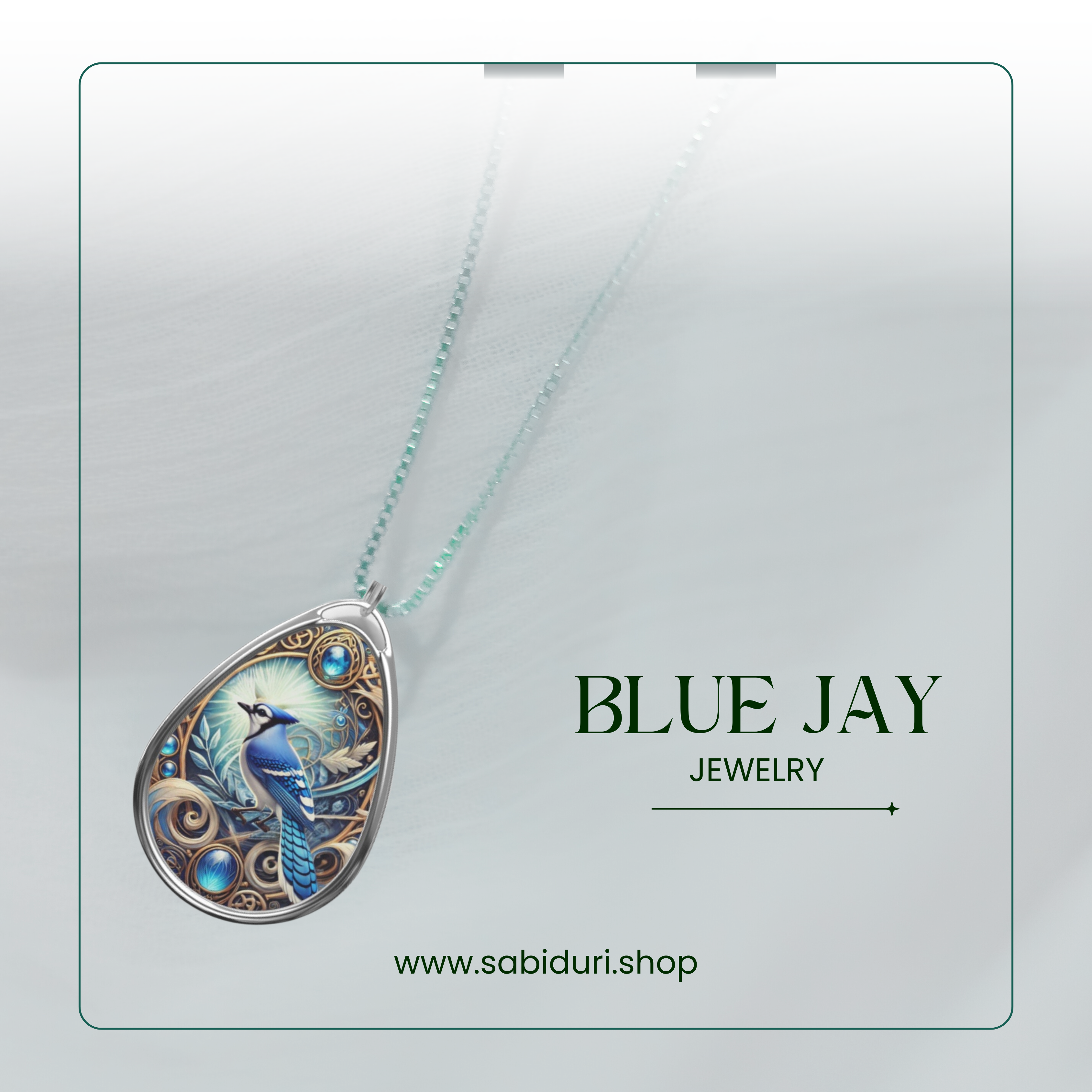 A close-up of a silver teardrop necklace pendant with a vibrant blue jay design and intricate blue gemstone details, set against a white, textured fabric. The text reads "BLUE JAY JEWELRY" with the URL "www.sabiduri.shop" below.