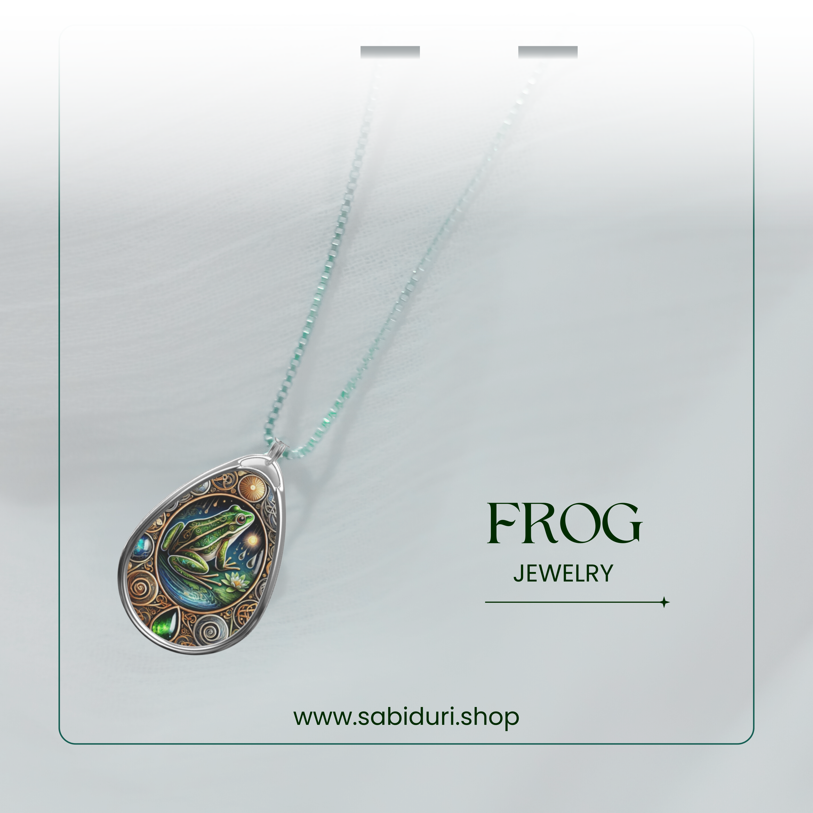 A softly lit product shot of the frog necklace, suspended against a white, textured background. The pendant’s deep greens and blues stand out, with "FROG JEWELRY" and "www.sabiduri.shop" text providing a refined branding touch.