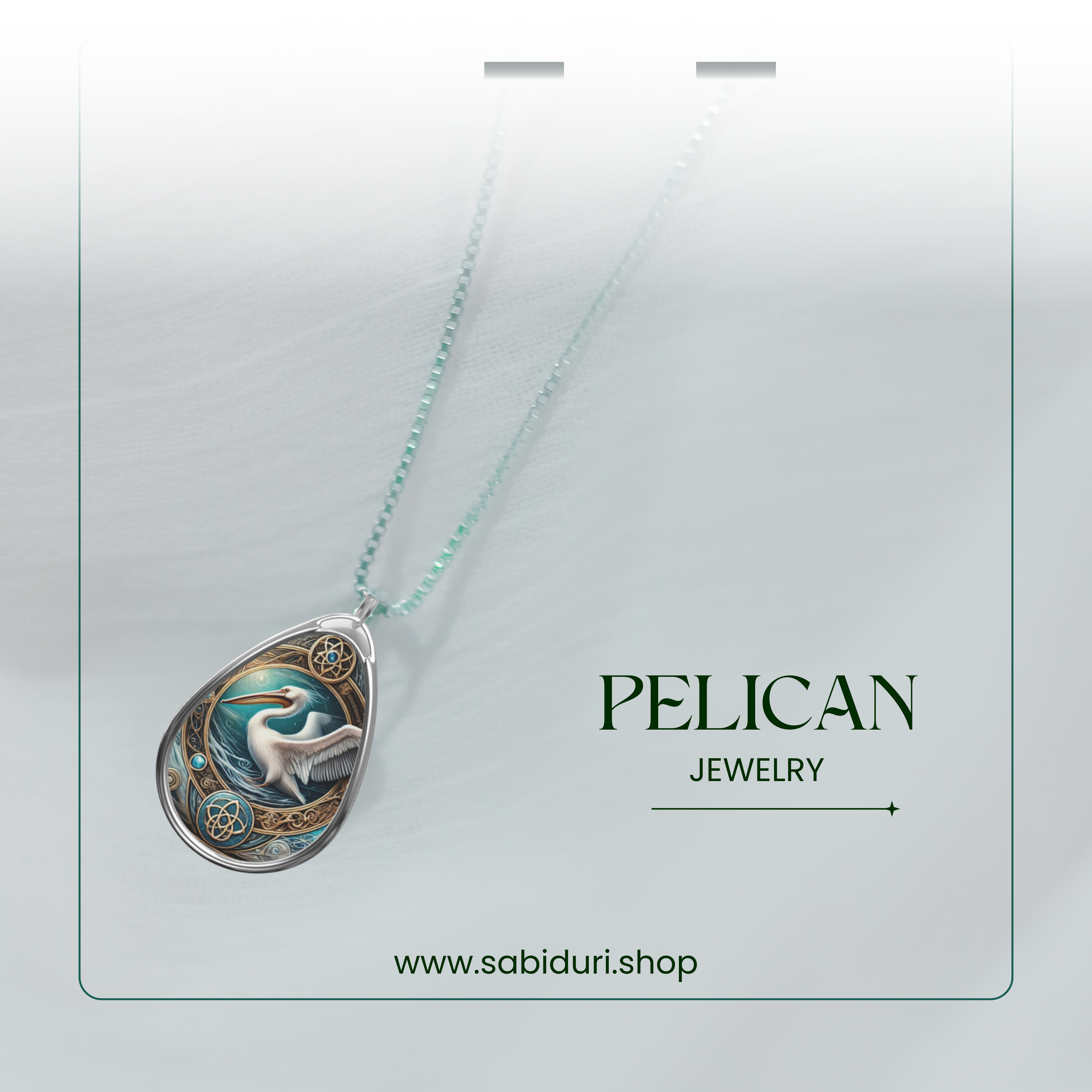A delicate silver chain suspends a teardrop-shaped pendant featuring a majestic pelican, adorned with gold filigree and blue embellishments, set against a soft white fabric. The website "www.sabiduri.shop" is displayed below.