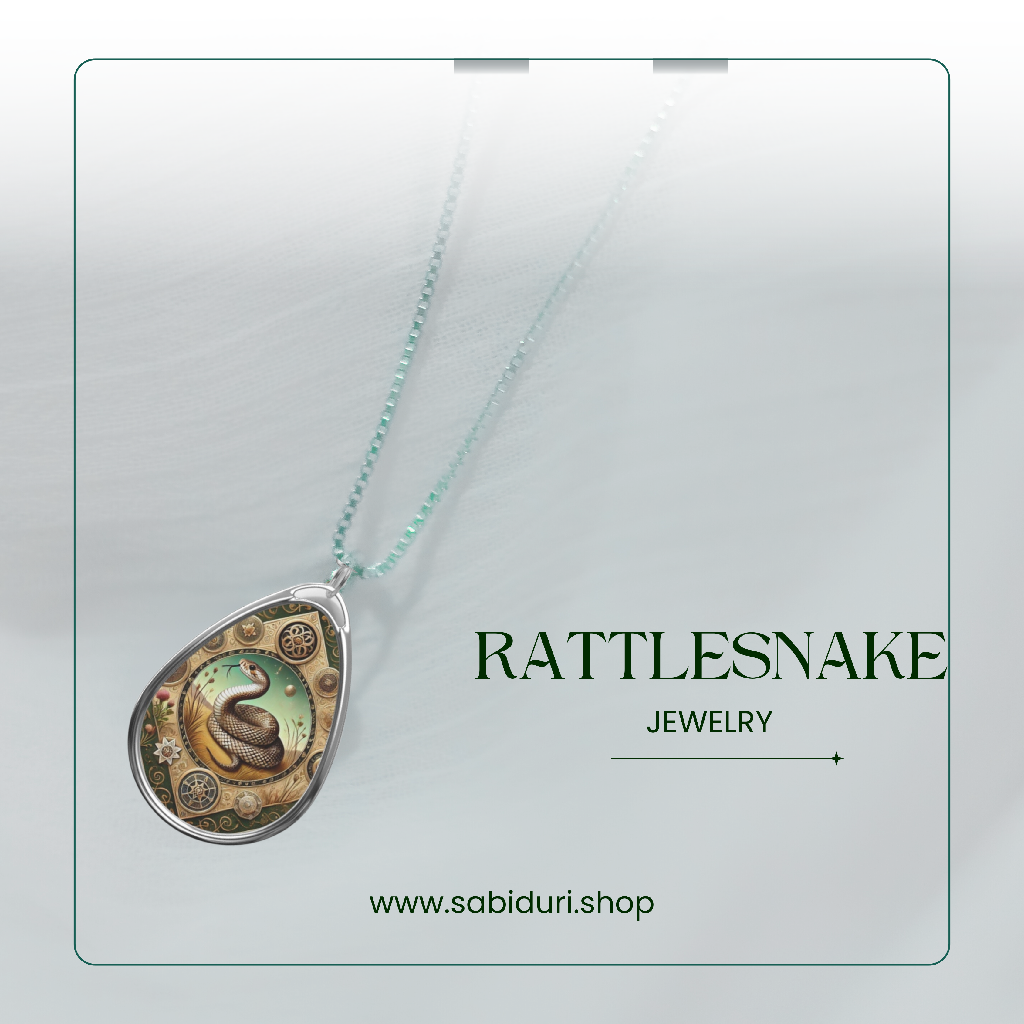 A teardrop-shaped necklace pendant with an intricate design of a rattlesnake coiled at the center, surrounded by gears and floral patterns in gold and green tones. The pendant hangs from a delicate chain on a soft, blurred background with the text "Rattlesnake Jewelry" and the website "www.sabiduri.shop" displayed.