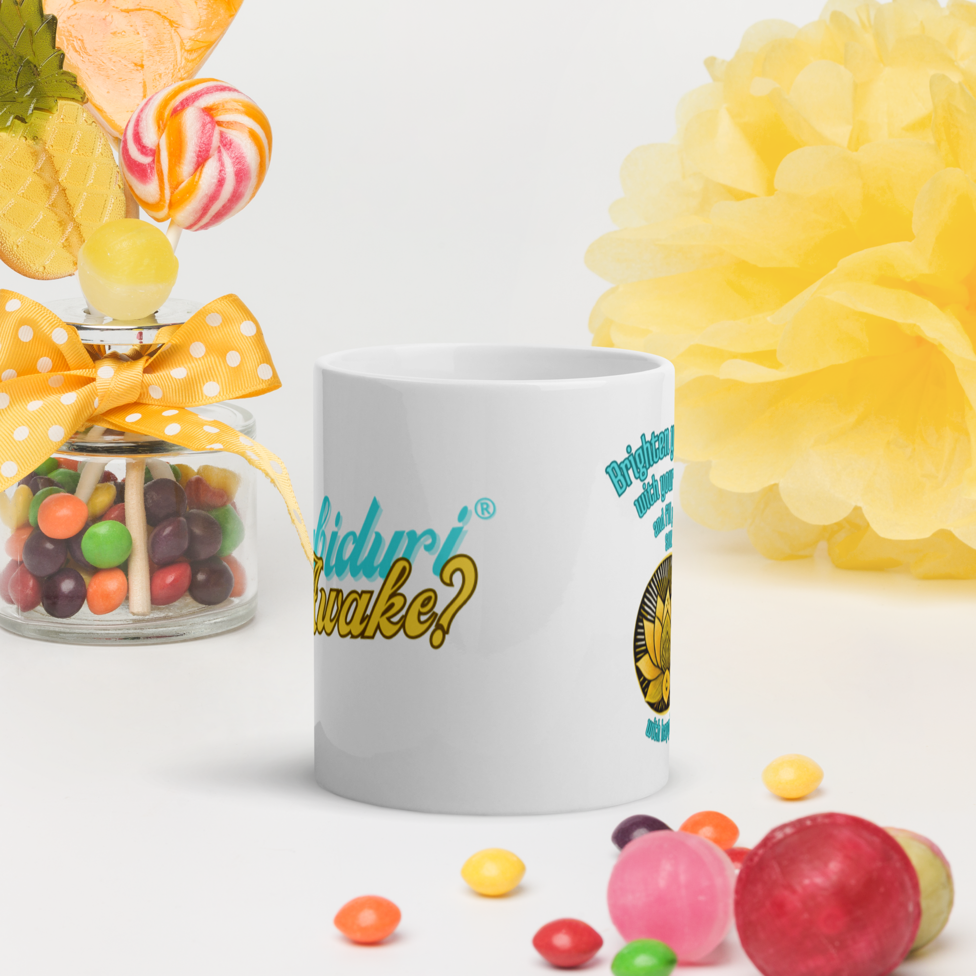 A white ceramic mug with the phrase "Sabiduría Awake?" in a bold, playful font. The mug is placed on a white surface with colorful candies and a decorative jar in the background.