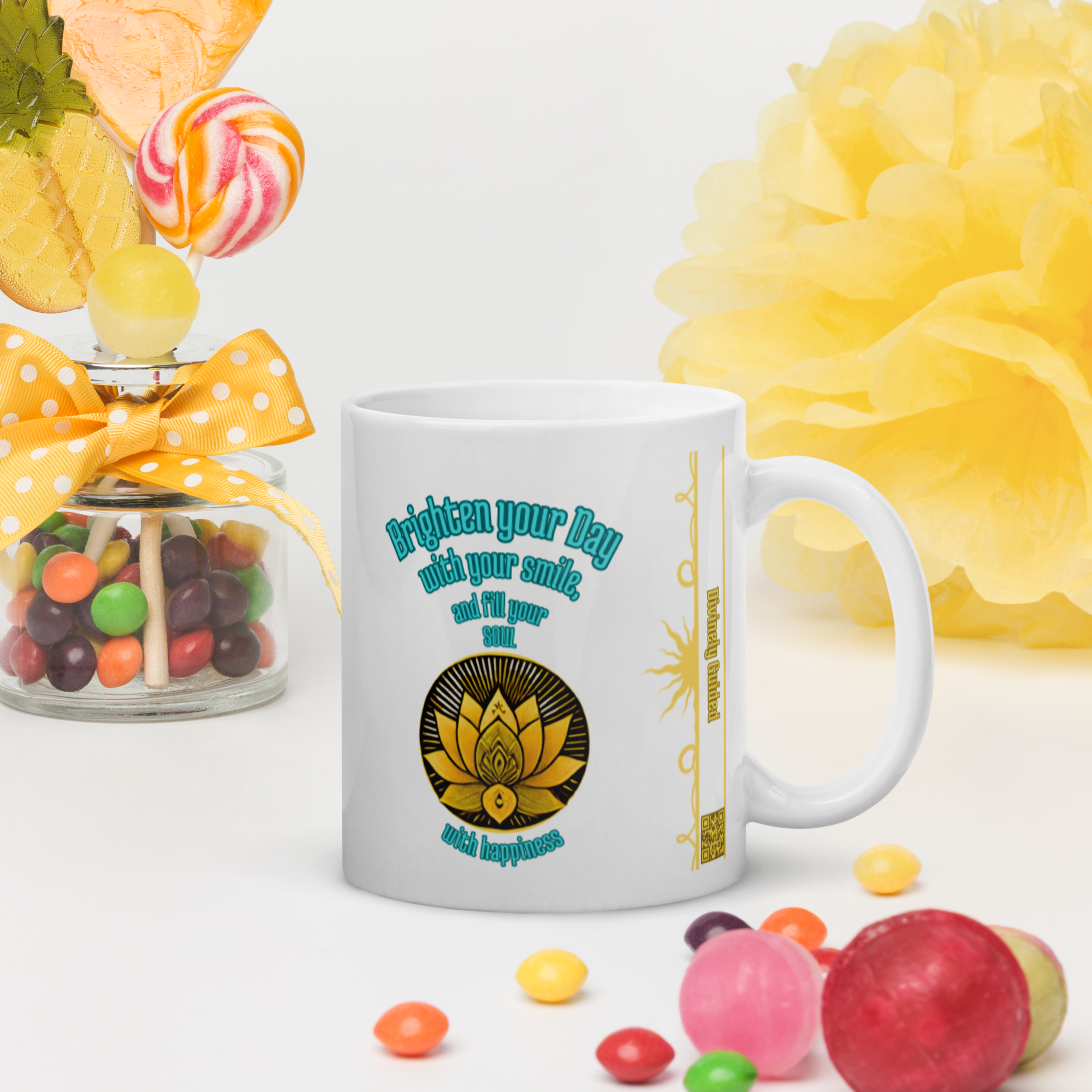 A white ceramic mug with a colorful design, featuring the phrase "Brighten your Day with your smile, and fill your soul with happiness" around a golden lotus symbol. The mug is placed on a white surface with colorful candies and a decorative jar in the background.