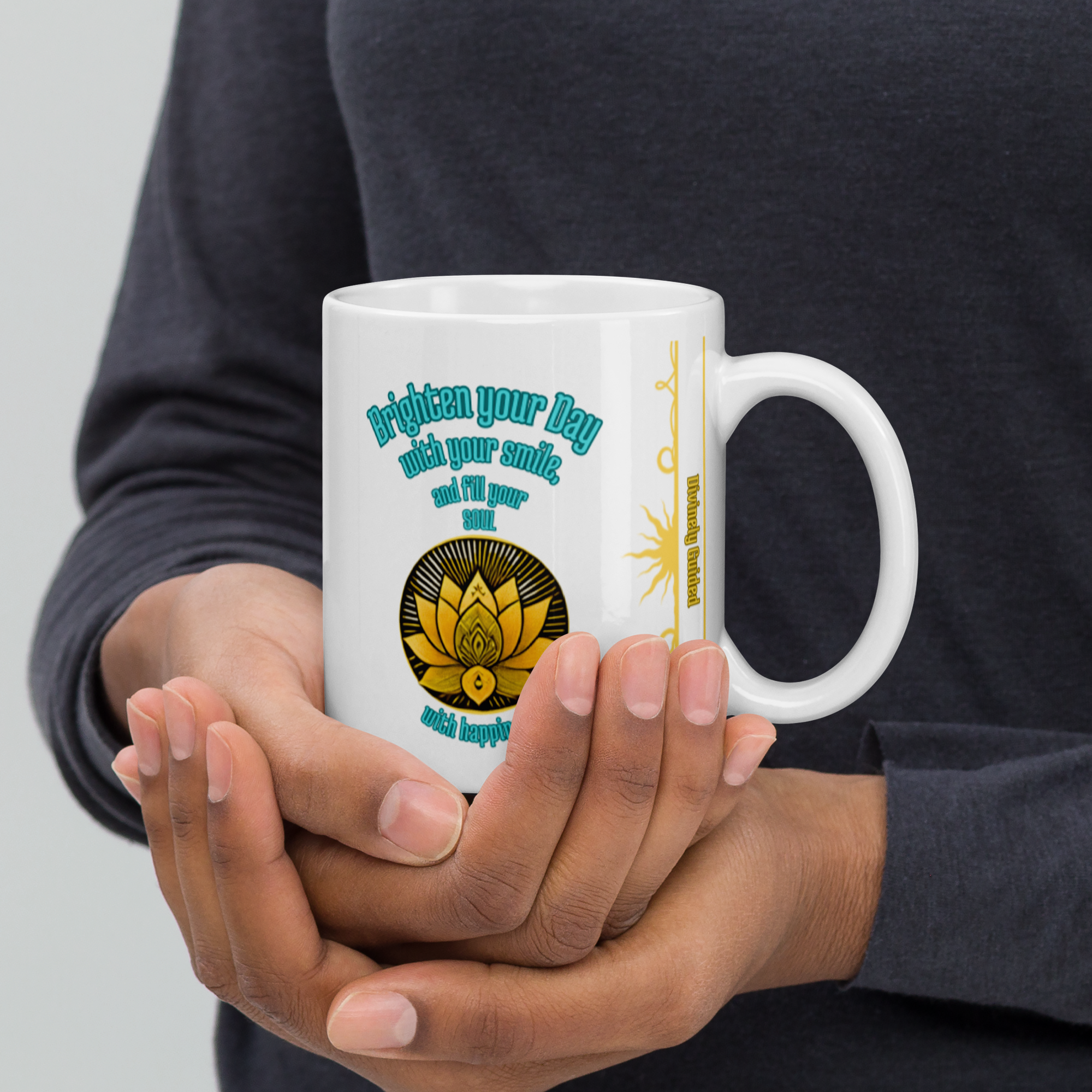 Hands holding a white mug with the same "Brighten your Day with your smile, and fill your soul with happiness" text and lotus design. The person is wearing a dark-colored shirt, highlighting the mug's vibrant design.