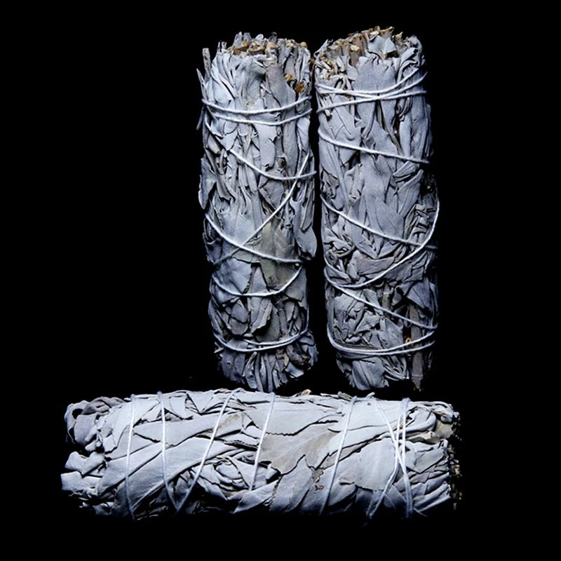 Three white sage bundles are shown against a black background. The sage bundles are tightly wrapped with string, highlighting the layered, overlapping leaves.